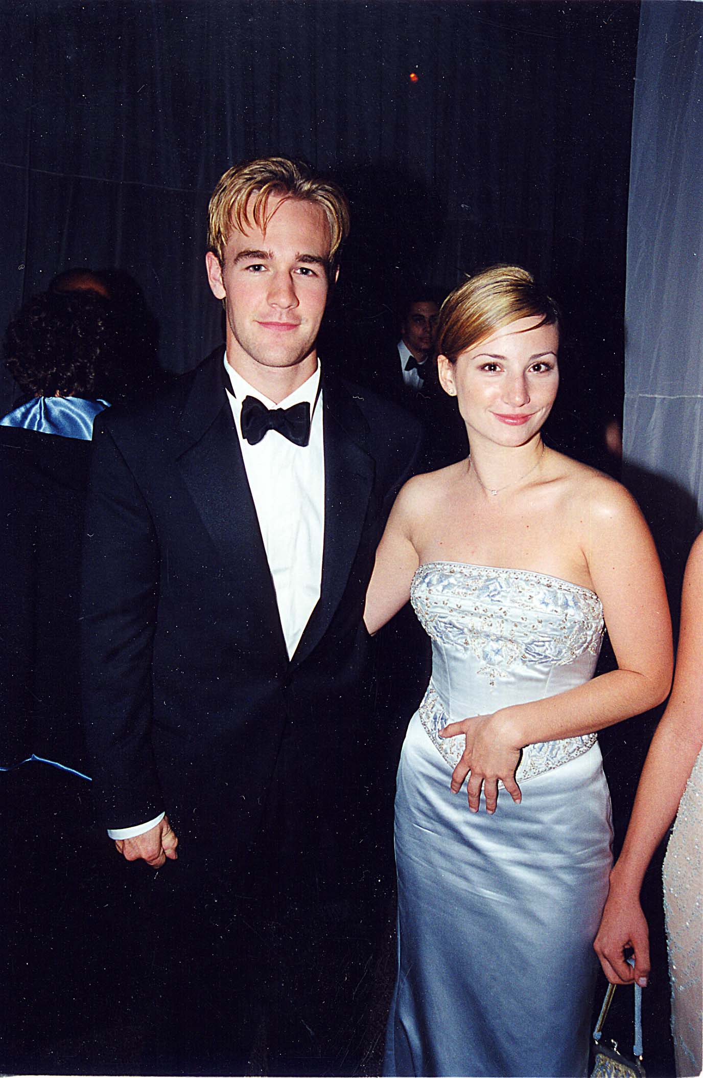 James Van Der Beek stands in a sharp black tuxedo and bow tie. Beside him, his date glows in a strapless ice-blue satin gown with intricate beaded embroidery along the bodice. Her sleek updo and minimal jewelry give her a polished, almost bridal elegance that complements his classic look.