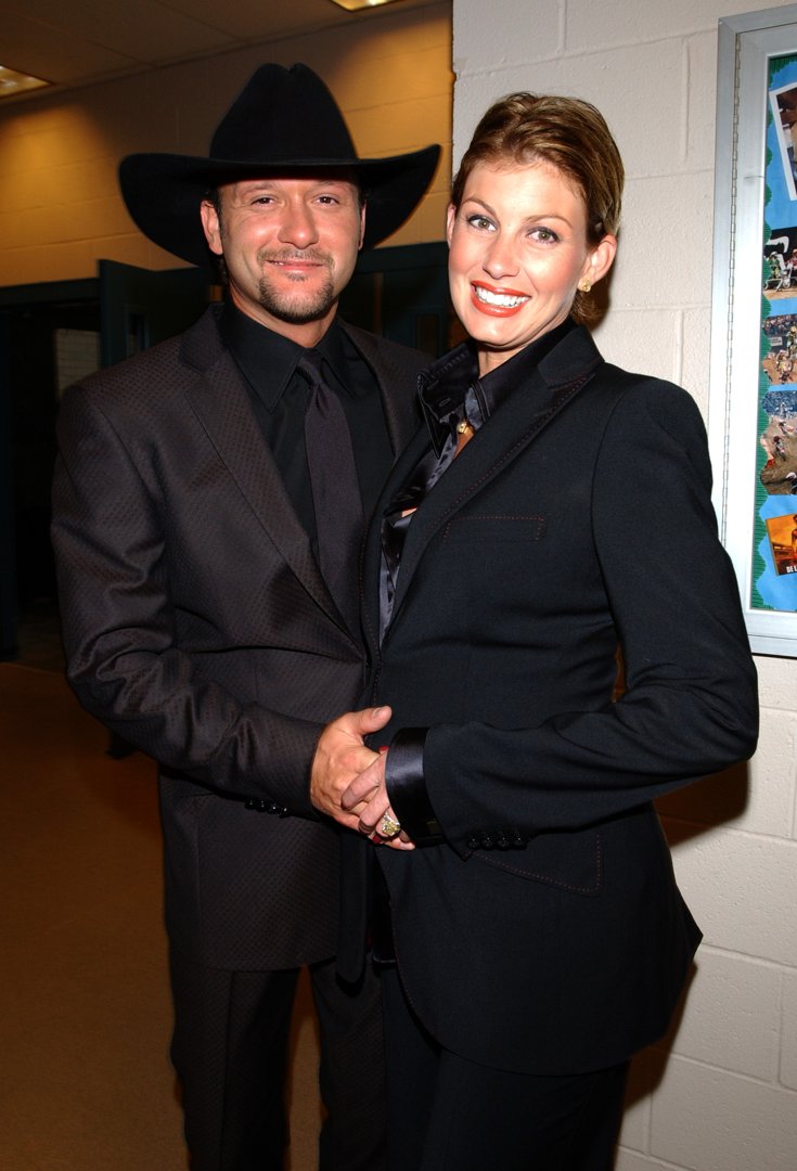 Backstage at Andre Agassi's Grand Slam fundraiser in Las Vegas, Tim McGraw and Faith Hill stand hand-in-hand, both in tailored black. Their polished look is all elegance, their pose close and quietly proud.