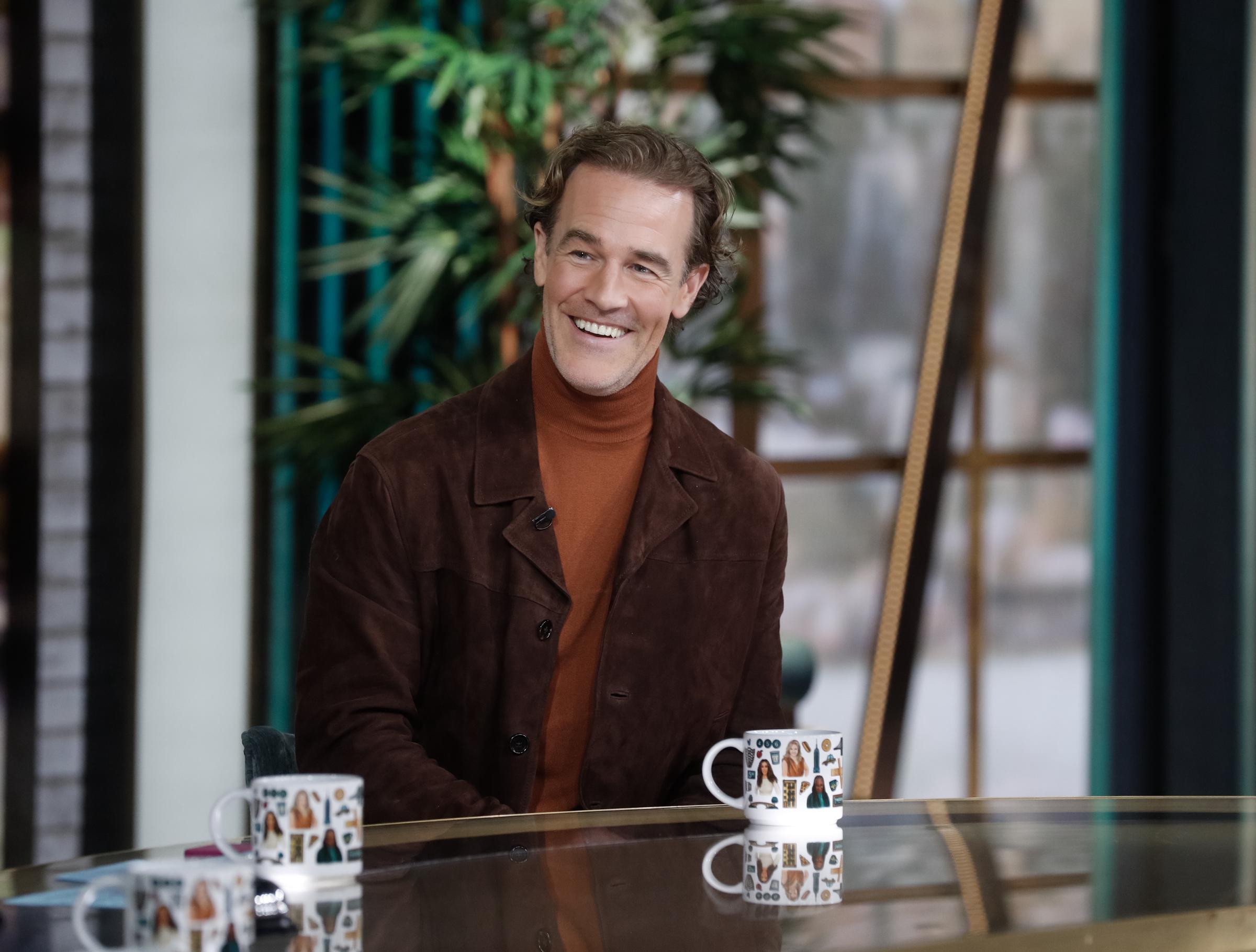 James Van Der Beek sits with easy warmth in a suede jacket and rust turtleneck, his smile lighting up 