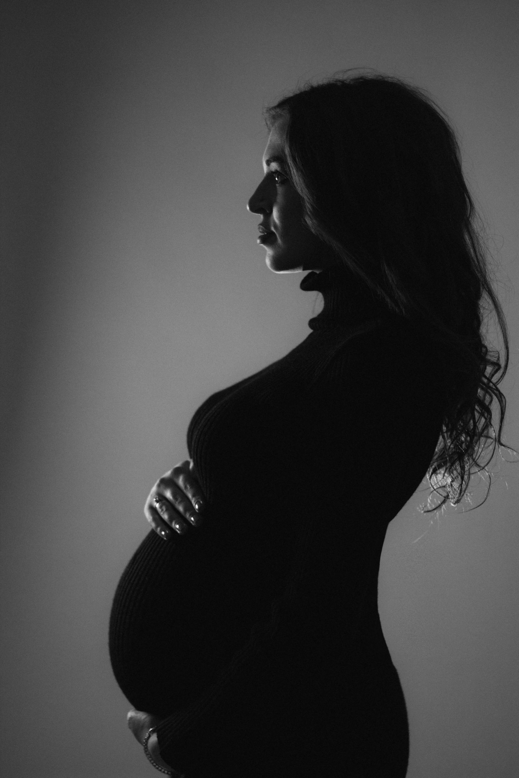 A black-and-white side-profile image of a pregnant woman holding her baby bump | Source: Pexels