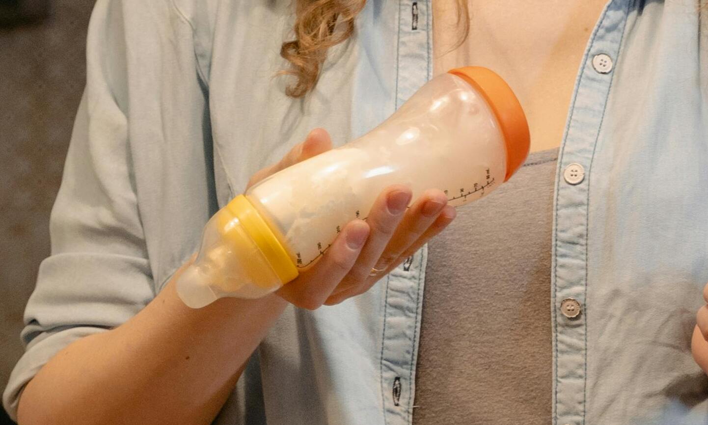 A woman in a denim shirt holding a baby bottle filled with milk | Source: Pexels