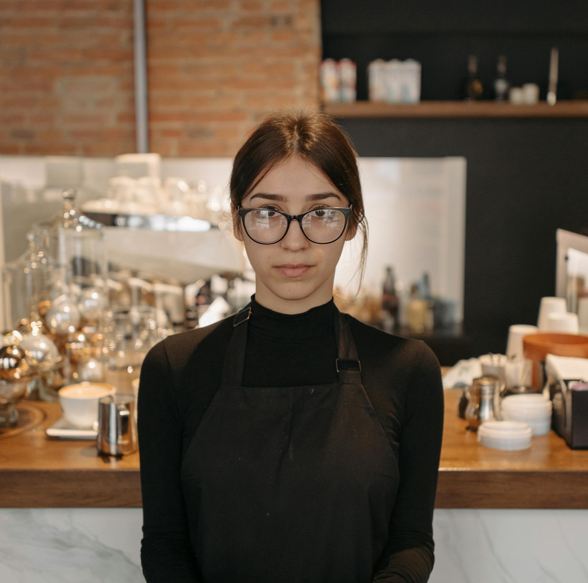 A waitress with glasses and an apron standing behind a counter in a café | Source: Pexels