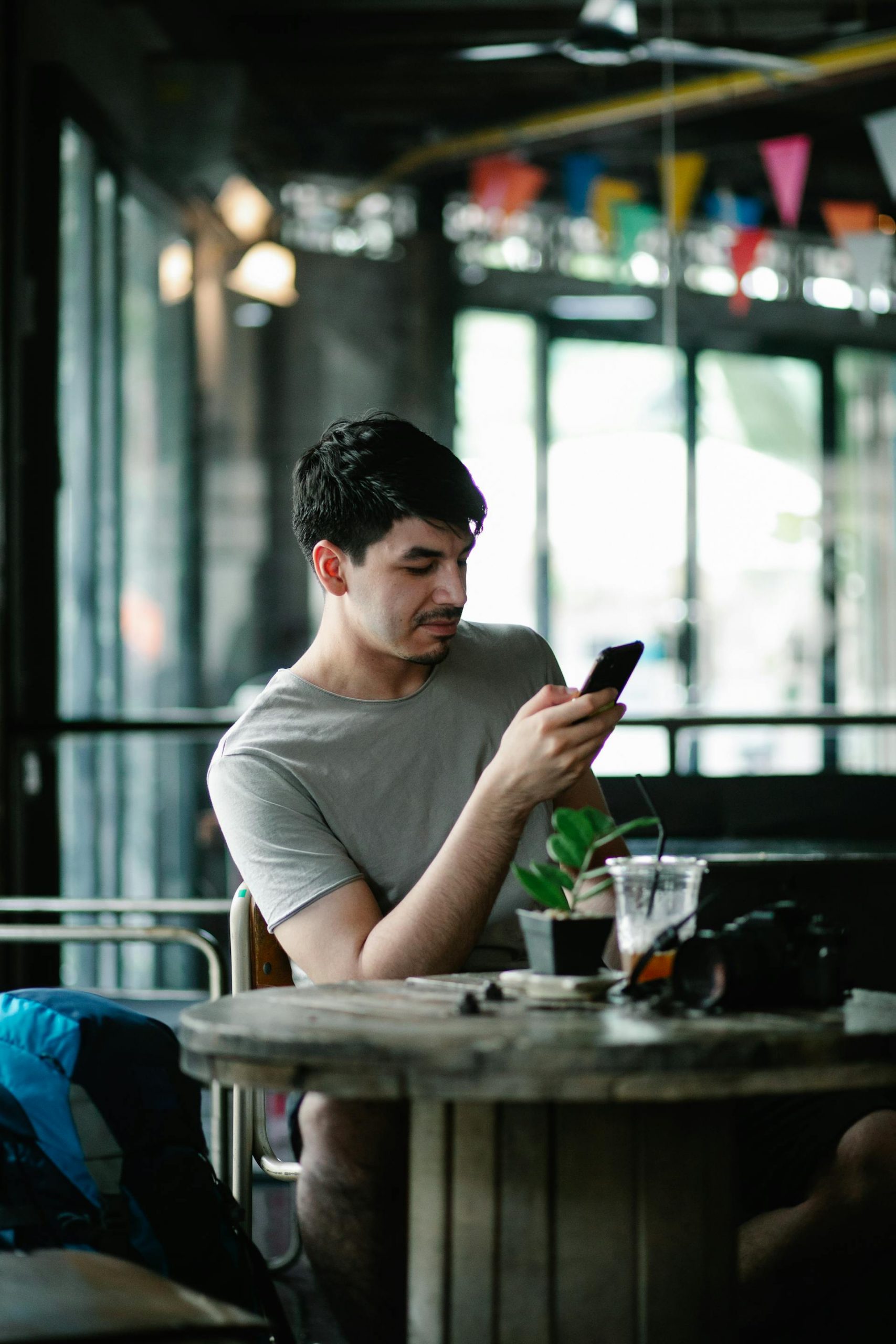 A man with dark hair in a gray shirt sitting at a table in a café looking at his phone | Source: Pexels