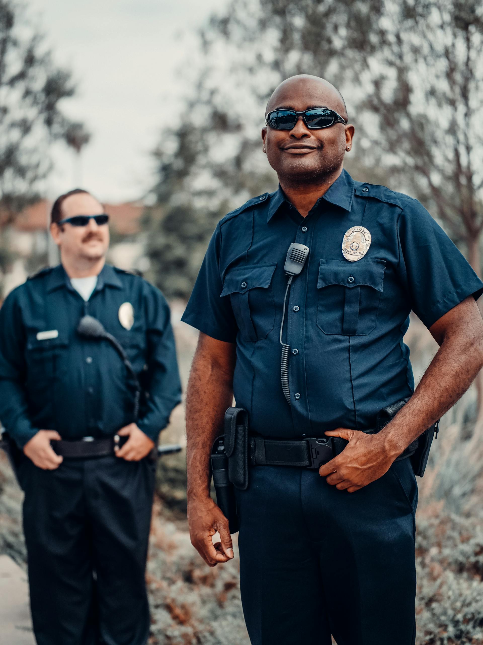 Two smiling police officers in uniform with sunglasses on | Source: Pexels