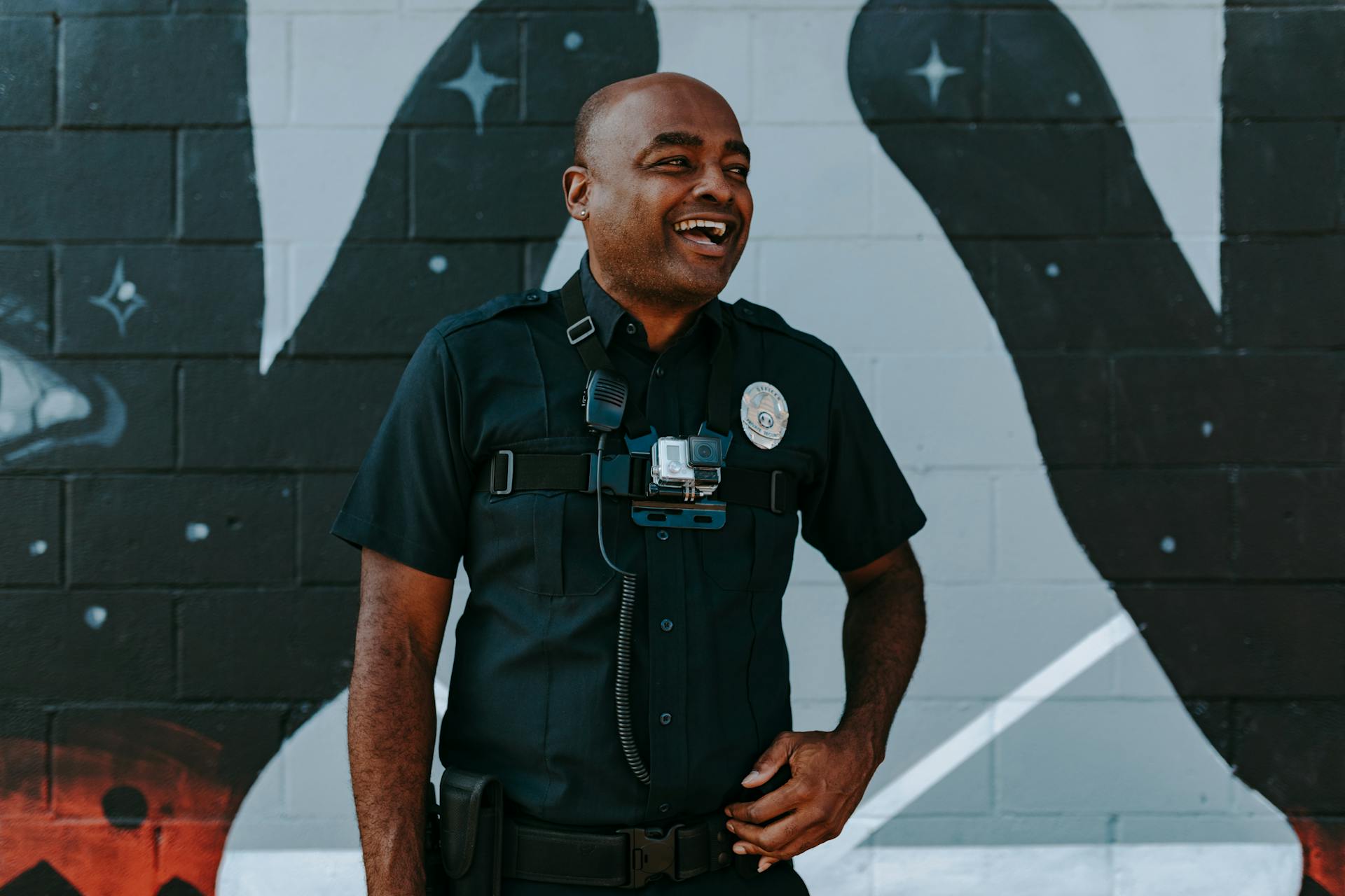 A police officer with a body camera laughing in front of a graffiti wall | Source: Pexels