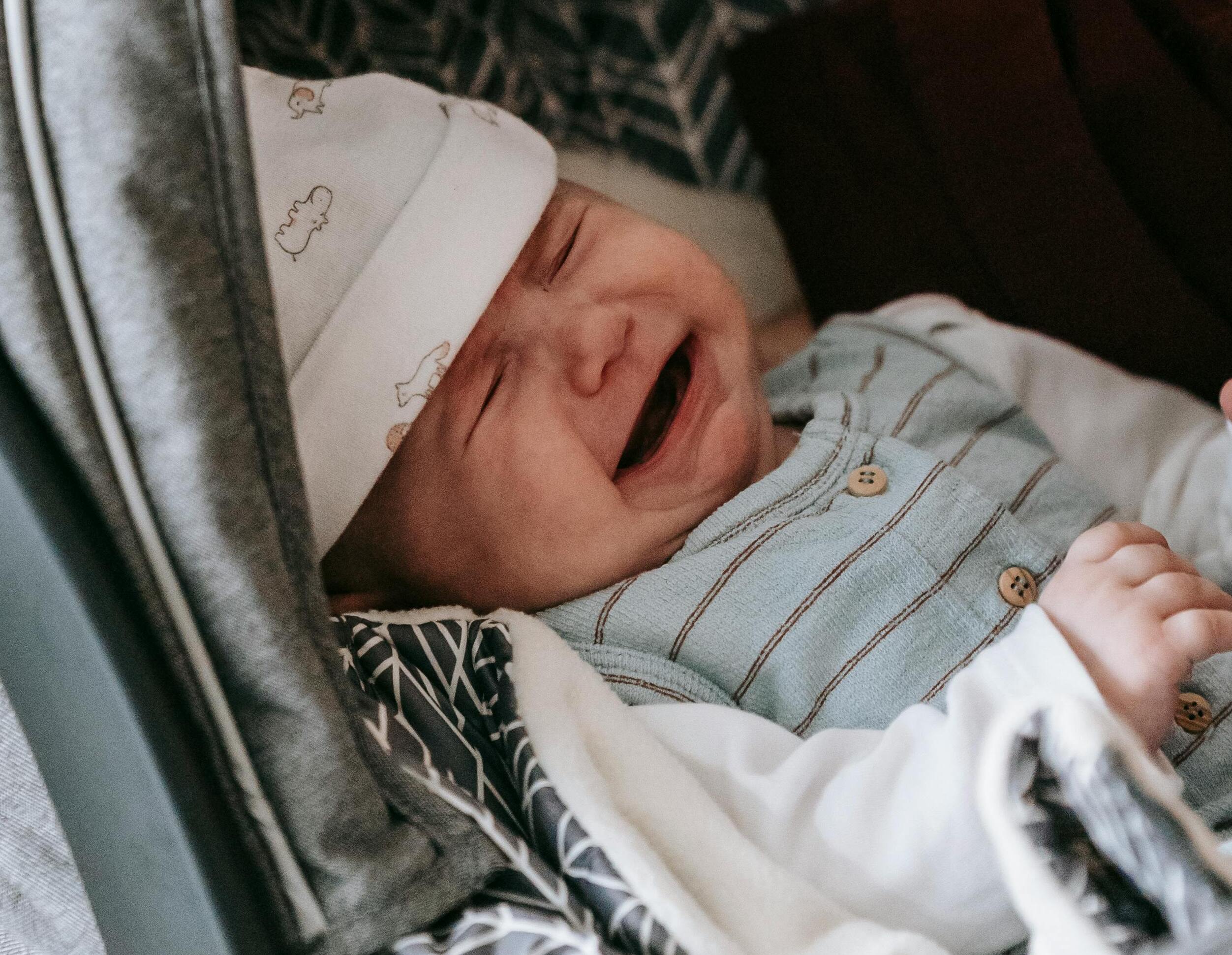 A baby in a striped onesie and a white hat, crying | Source: Pexels