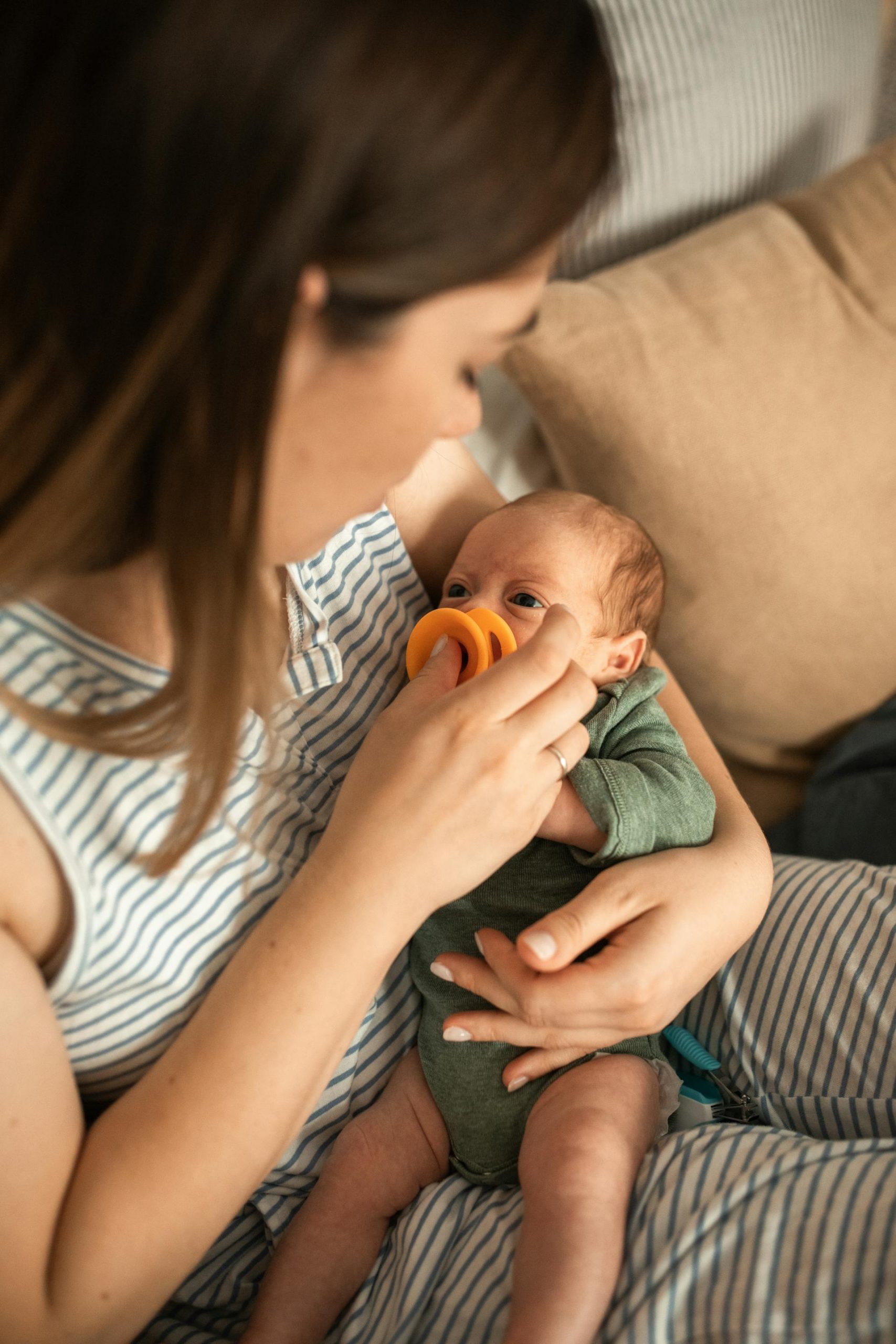 A mother in a striped top holding her baby while giving it a pacifier | Source: Pexels