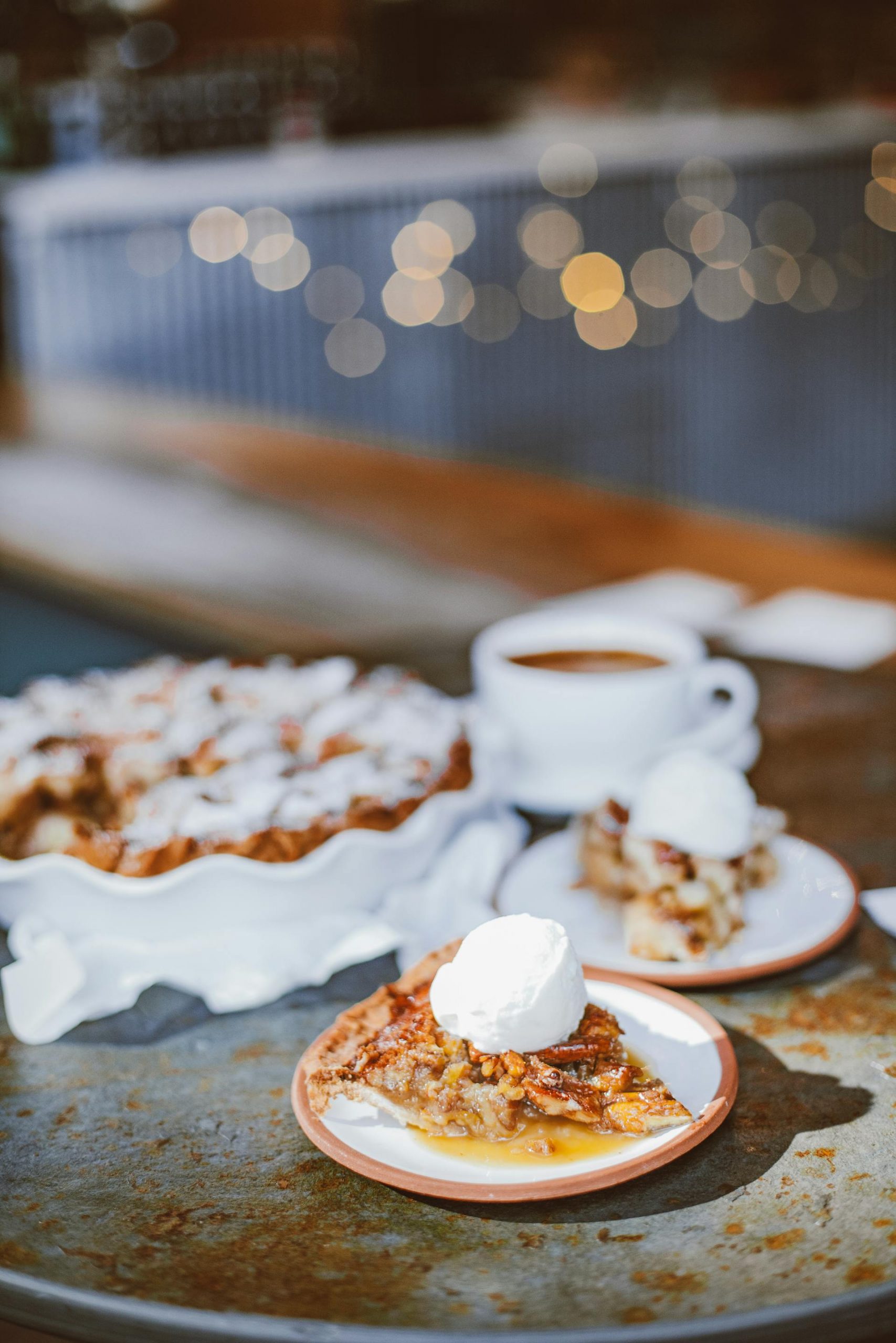 A dessert pie topped with a scoop of ice cream on a table with a cup of coffee and string lights in the background | Source: Pexels