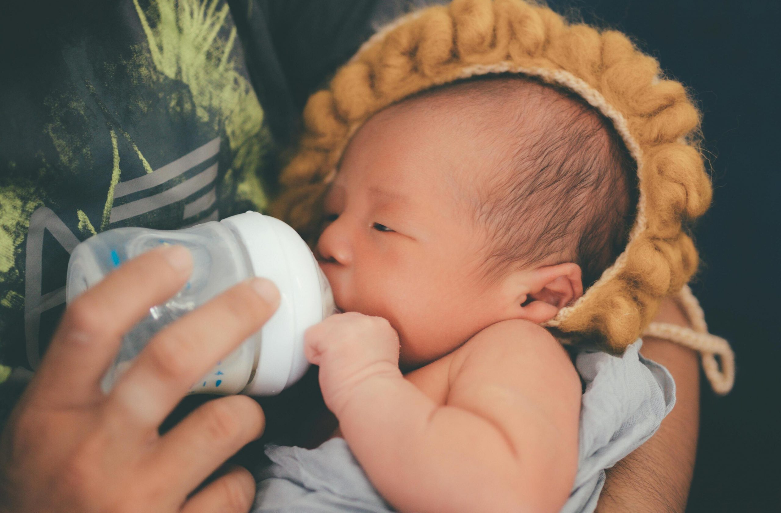 A person feeding a newborn baby with a bottle while the baby is wearing a cute lion hat | Source: Pexels