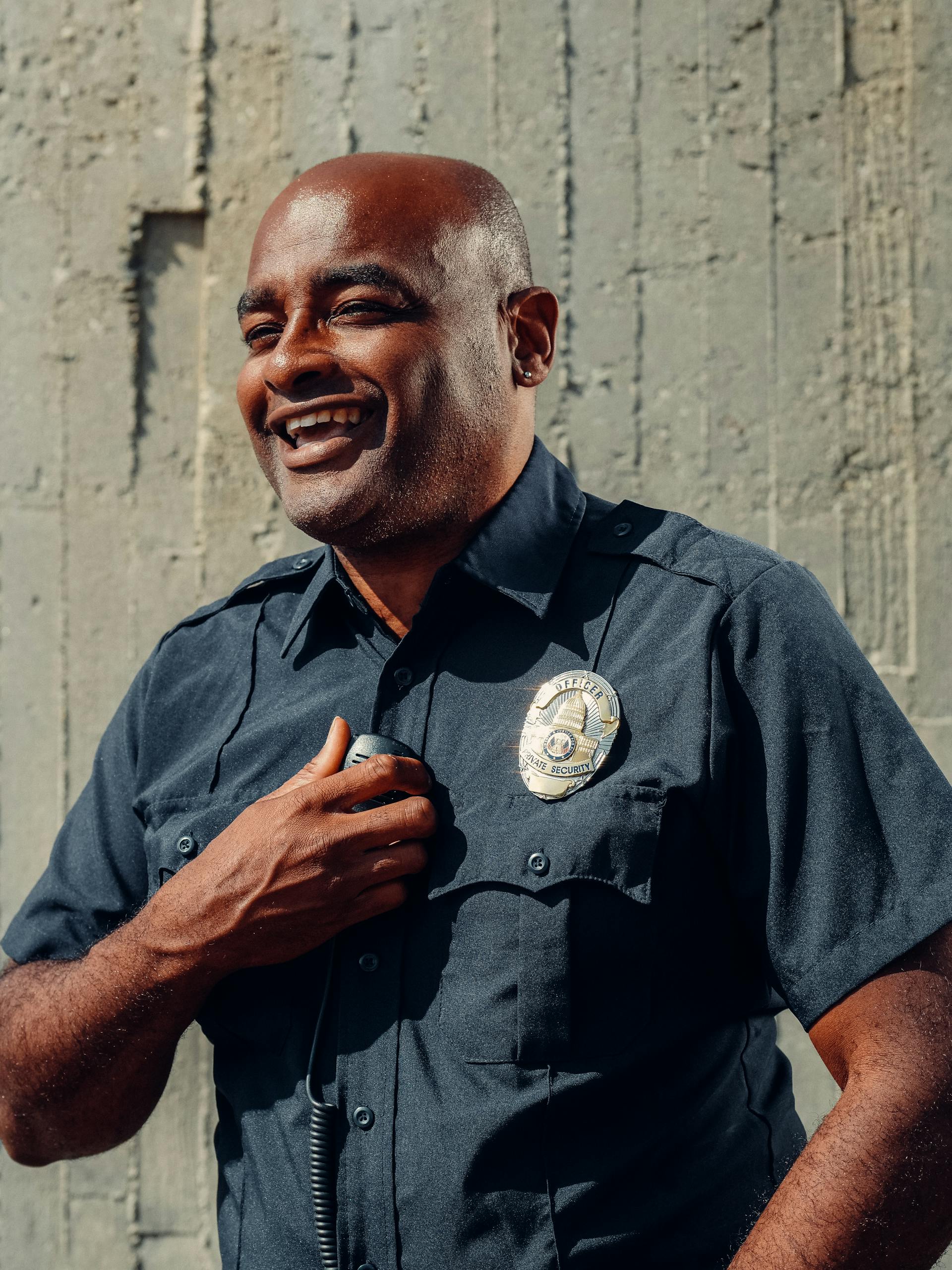 A smiling police officer holding a radio while standing in front of a gray wall | Source: Pexels