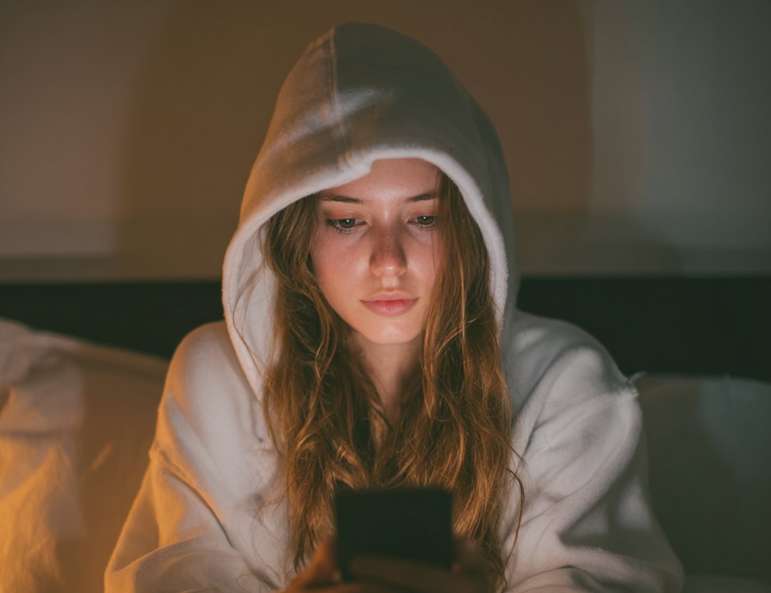 A woman sitting on her bed and using her cellphone | Source: Midjourney
