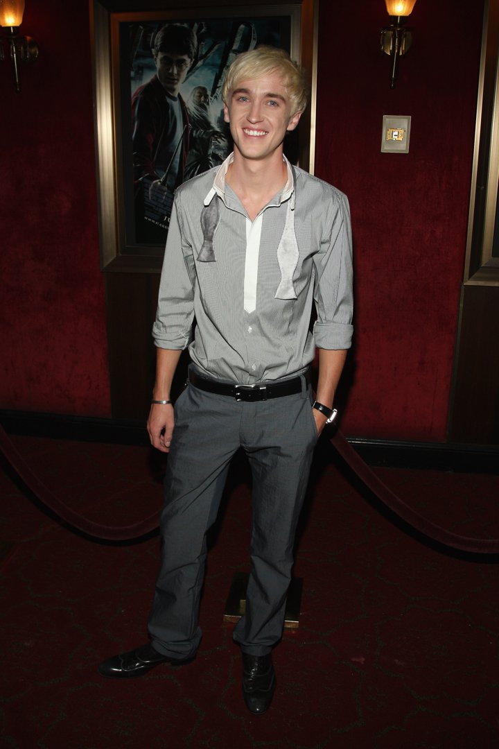 Tom Felton stands with an easy grin, his undone bow tie giving him a charmingly relaxed, post-premiere glow. The silver tones of his outfit echo the moody magic of the film promoted just behind him. It's a moment that captures youthful confidence, red-carpet ease, and a hint of Draco Malfoy mischief left over from the screen.