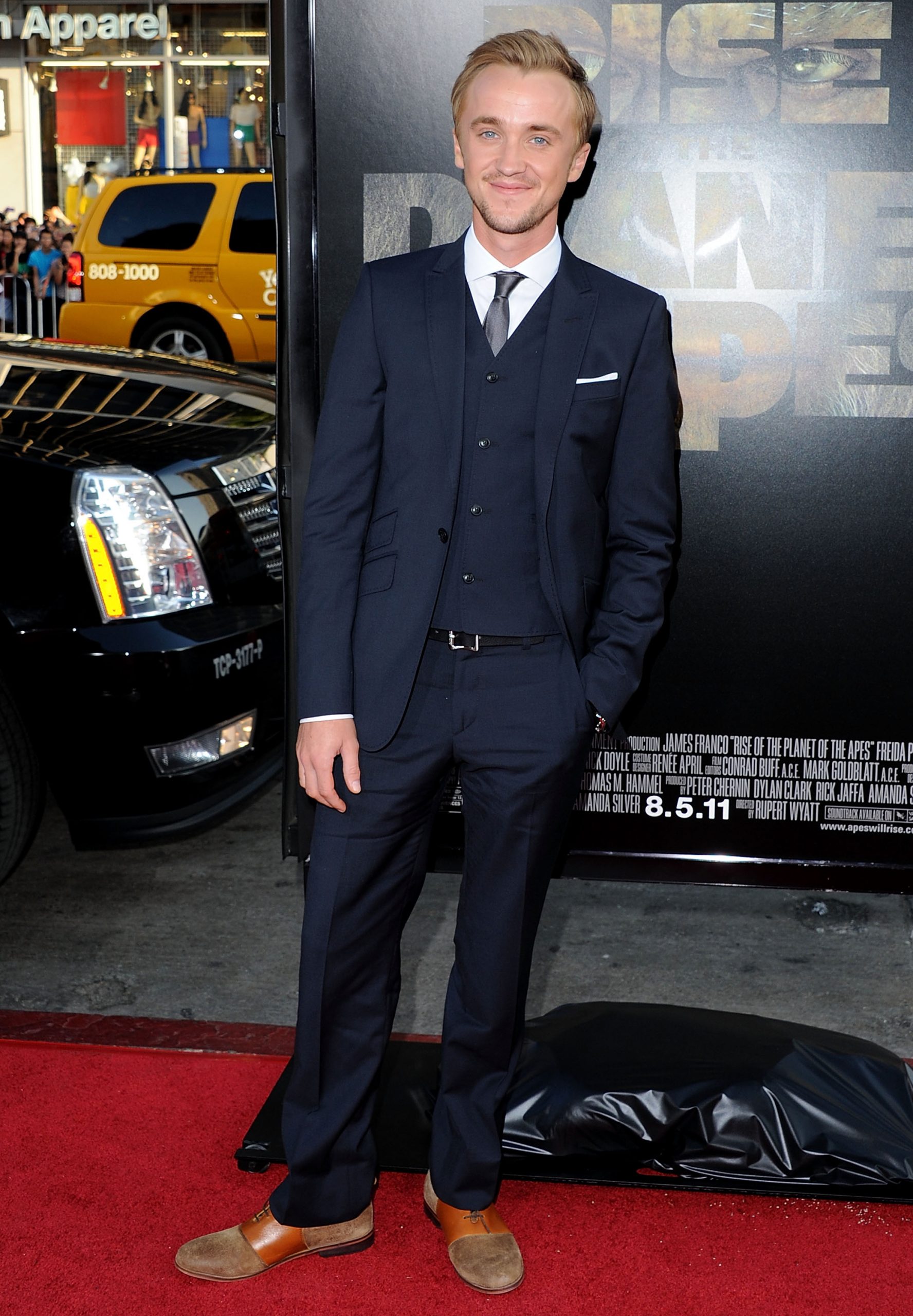 Tom Felton steps onto the red carpet in a sleek navy suit, looking effortlessly polished against the Hollywood buzz. With a calm smile and hands casually at his sides, he brings a touch of understated charm to the high-energy premiere. Set before the bold backdrop of the 