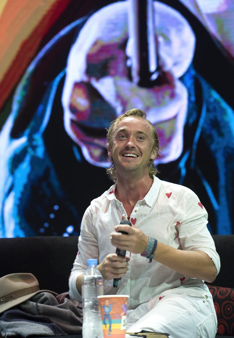 Tom Felton beams under the bright stage lights, his heart-patterned shirt matching the warmth of his smile. With a microphone in hand and an excited crowd before him, he radiates easy going charm and enthusiasm. At Argentina Comic-Con in Costa Salguero, he appears completely at home among fans who adore him.