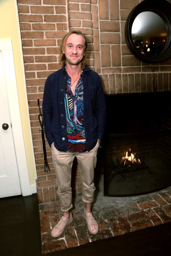 Tom Felton stands by a glowing fireplace, his vibrant patterned shirt adding a burst of color to the cozy setting. With a relaxed smile and hands tucked into his pockets, he exudes an effortlessly bohemian charm. At the Celebration of YouTube Originals, he blends warmth and style as naturally as the flames behind him.