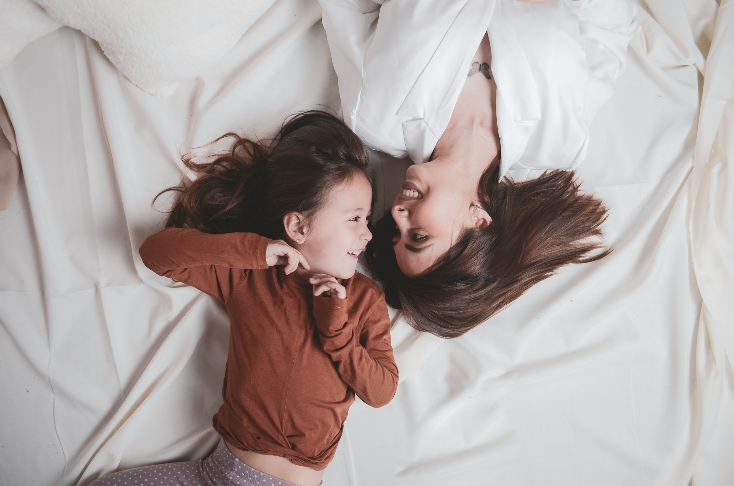 A woman and a little girl look at each other while lying on a bed | Source: Unsplash