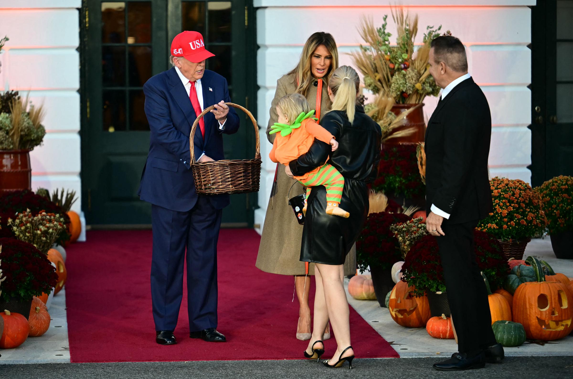 President Donald Trump and First Lady Melania hand out treats to Press Secretary Karoline Leavitt holding her son as husband Nicholas Riccio looks on during a Halloween event at the White House in Washington, DC, on OCtober 30, 2025. | Source: Getty Images