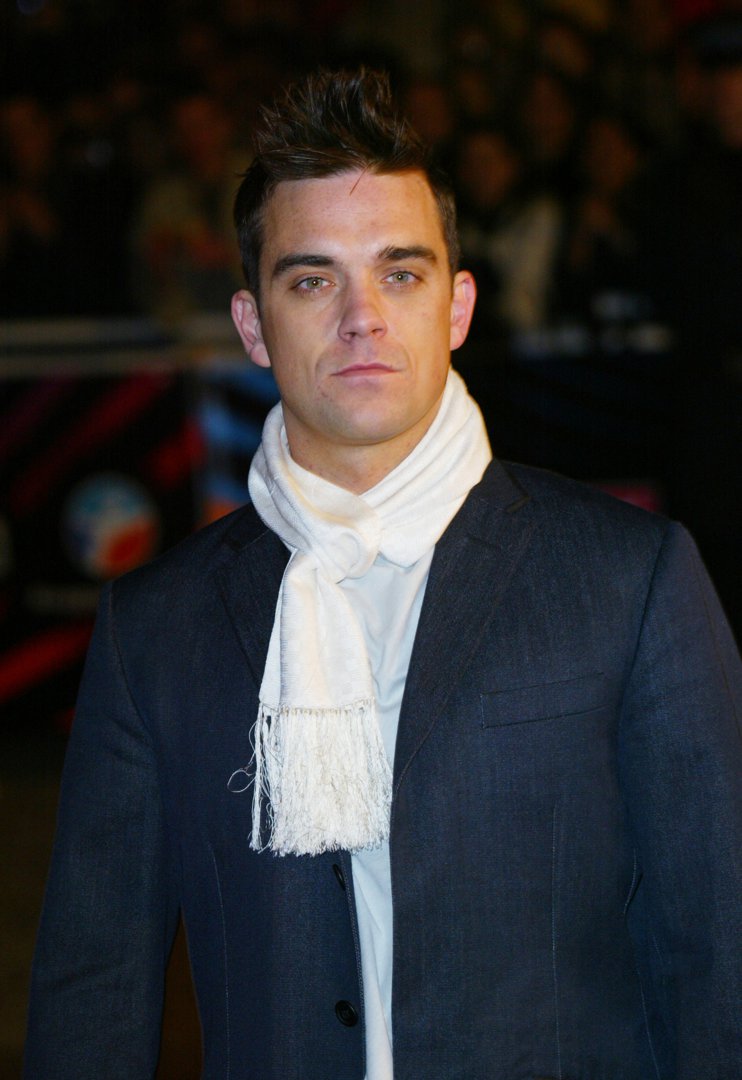Robbie Williams attended the NRJ Music Awards in Cannes, France, in 2003, dressed in a tailored suit and white scarf. With a sleek look and serious expression, he embodied the polished confidence of a pop star at the peak of his international fame.