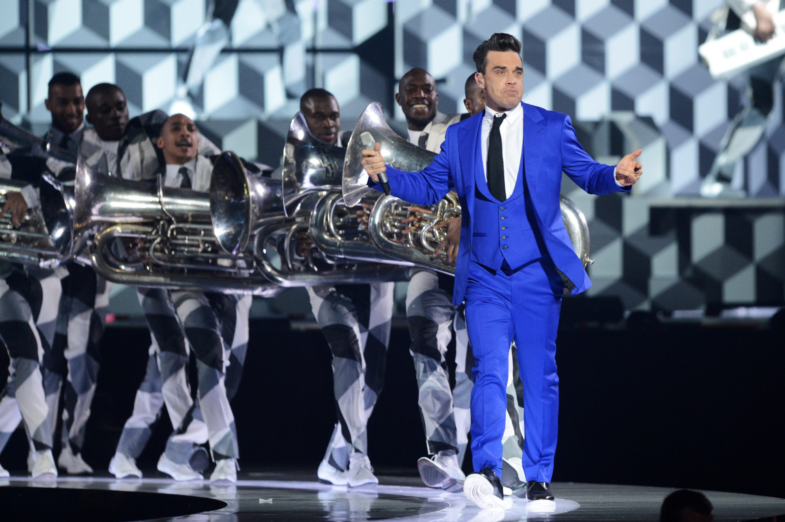 Robbie Williams performed at The Brit Awards 2013 on February 20 in London, England, wearing a striking electric-blue suit. Flanked by a brass band in bold black-and-white patterns, he delivered one of the night's most visually dynamic and energetic sets.