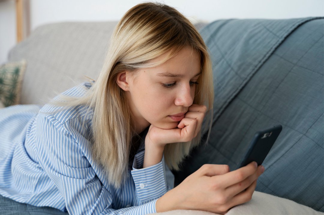 A sad teenage girl lying on the couch and looking at her phone | Source: Freepik