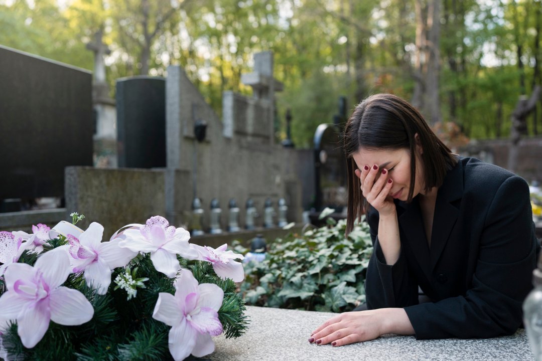 A woman mourning beside a grave in a cemetery | Source: Freepik