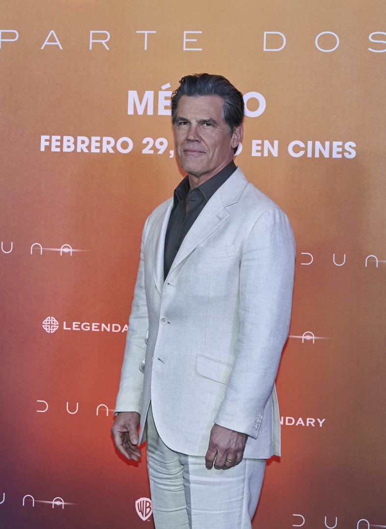 Wearing a light beige suit over a dark open-collar shirt, he appears clean-shaven with short, slicked-back hair and no visible tattoos — a refined and composed look that hints at reinvention.