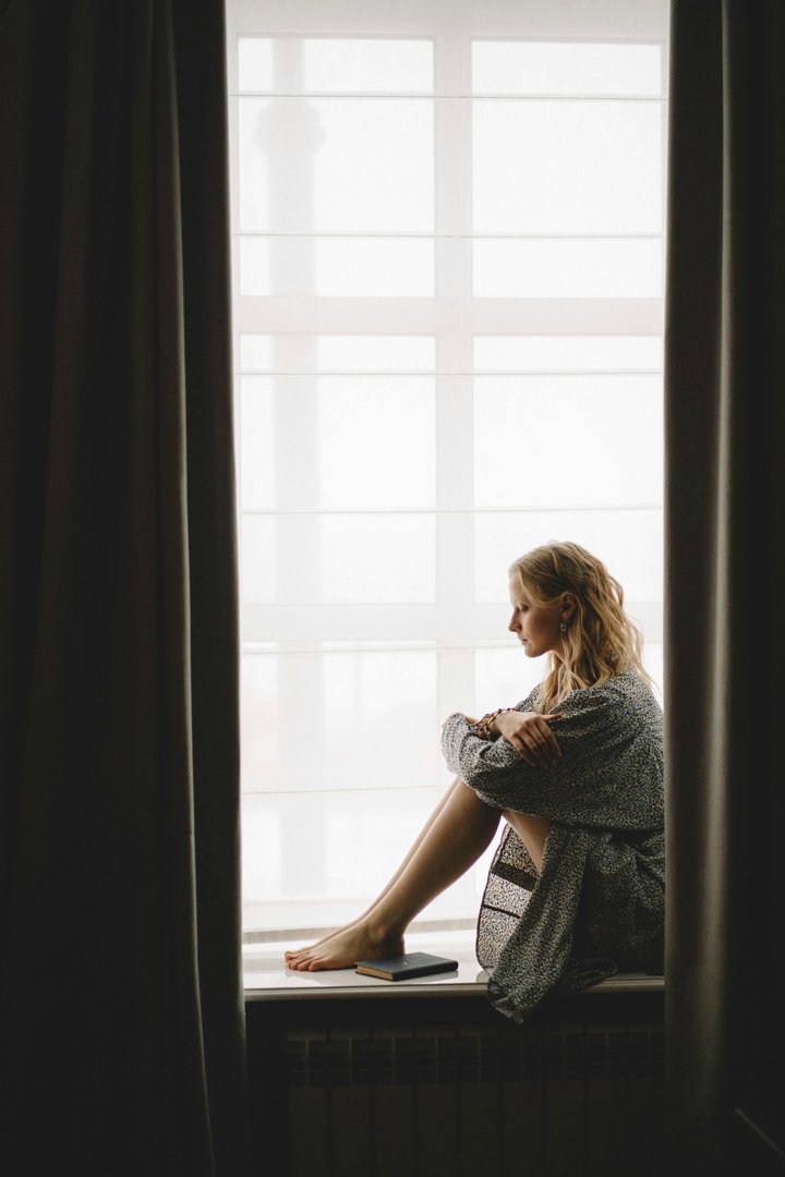 Stressed woman sitting on windowsill | Source: Pexe;s