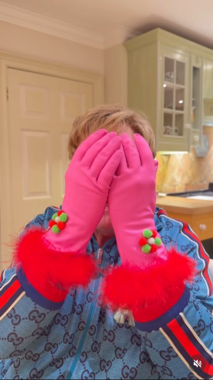 With a dramatic reveal of hot pink, faux-fur–trimmed cleaning gloves, John teases the chaos to come — a fabulously camp warning that he's about to take matters, and his oven, into his own hands. | Source: Instagram/eltonjohn