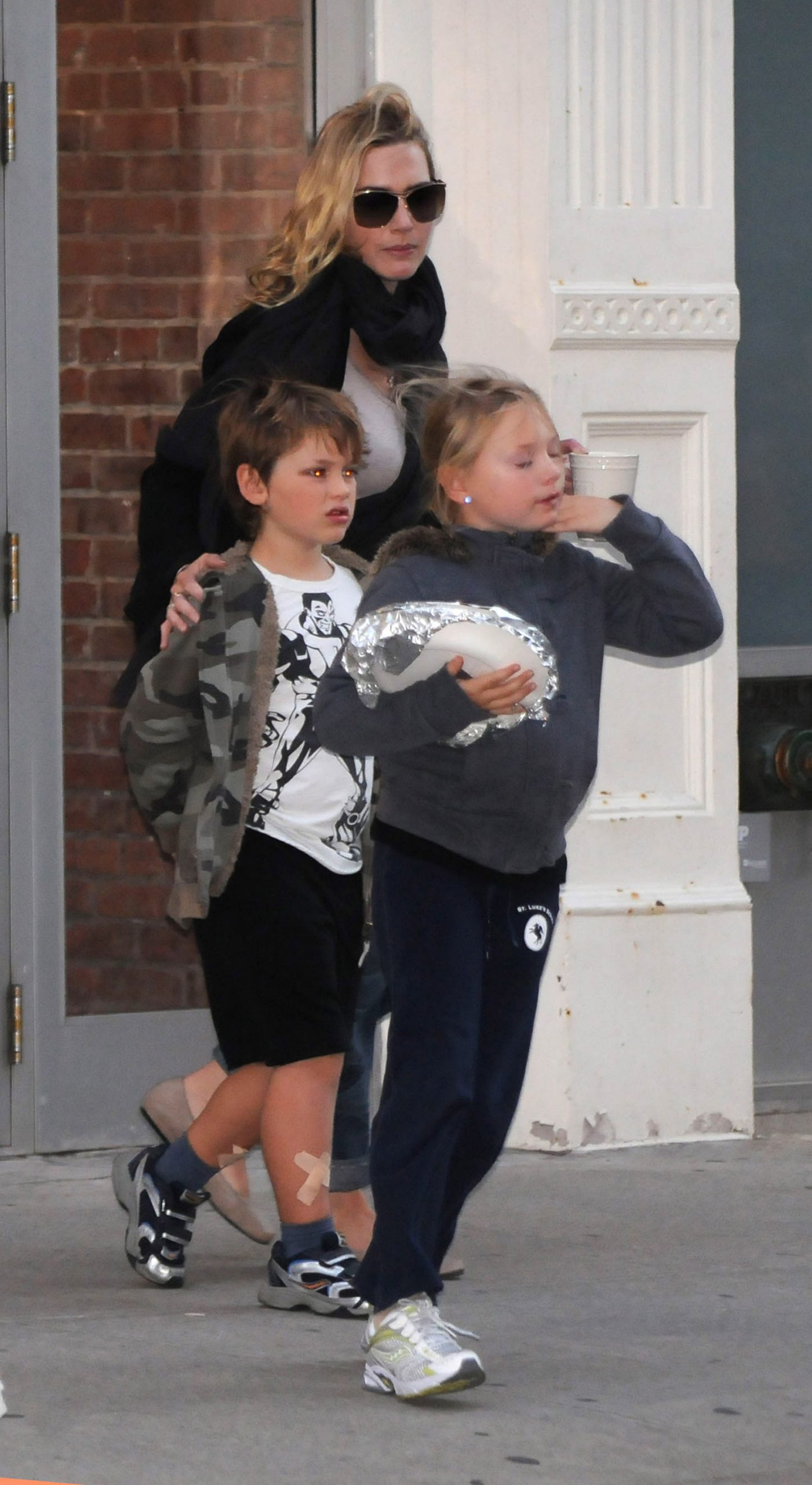 Kate Winslet was spotted in Manhattan on October 7, 2010, with her two children, Mia Honey Threapleton and Joe Alfie Winslet Mendes, during a casual family outing. Threapleton, carrying a foil-wrapped item and wearing school sportswear, led the way with purpose while Mendes, in a superhero T-shirt and visible plasters on his legs, stayed close — capturing a rare public glimpse of the trio navigating everyday life in New York City.