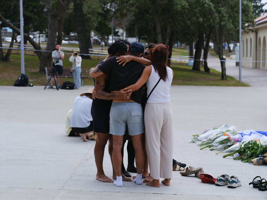 Mourners embraced near a growing sea of floral tributes left for the victims of the Bondi Beach shooting. Pairs of shoes, candles, and handwritten notes lay scattered on the pavement &mdash; quiet markers of a community united in sorrow and solidarity.