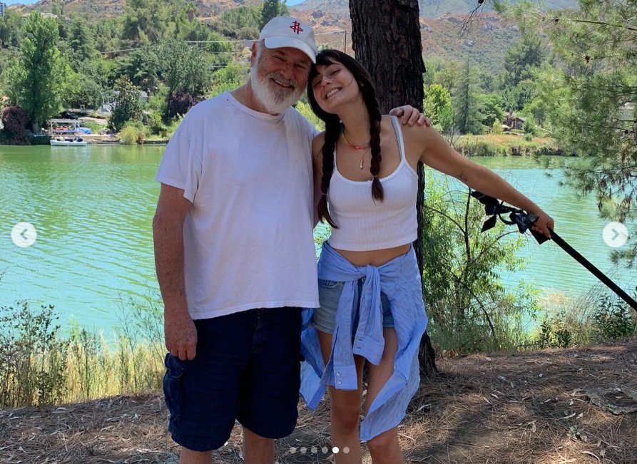 An outdoor photo shows Rob Reiner and his daughter Romy standing close together beside a lake surrounded by trees and hills, from a post dated March 6, 2022. | Source: Instagram/romyreiner