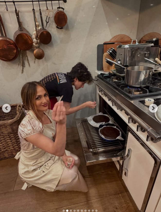 Jennifer Lopez holds a pick while the person behind her checks the cake in the oven, as seen from a post dated November 28, 2025. | Source: Instagram/jlo