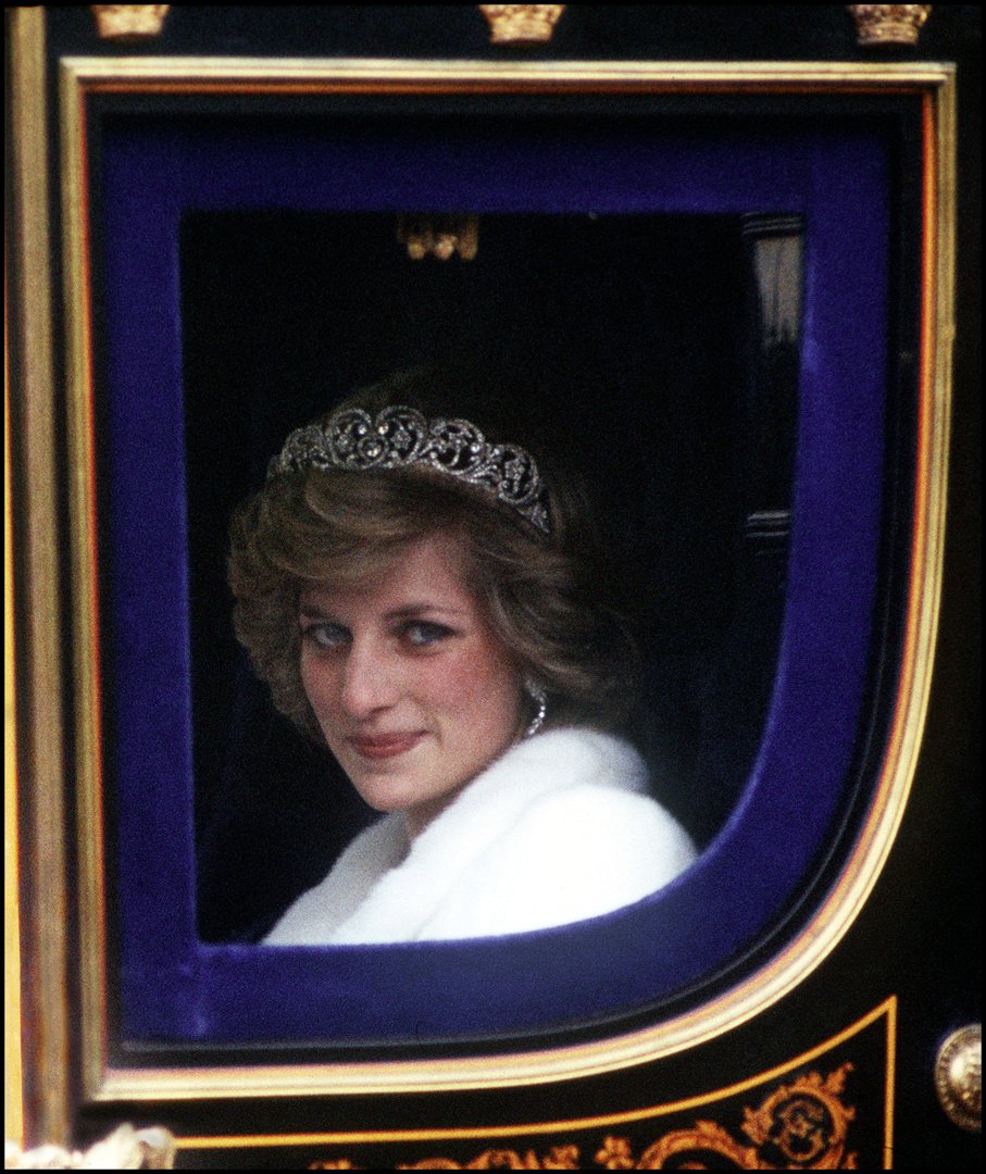 Princess Diana, radiant in a white fur coat and the famed Spencer tiara, rides in regal splendor to the State Opening of Parliament in November 1982. The young Princess of Wales joins Queen Elizabeth II in one of her earliest ceremonial roles as a senior royal.