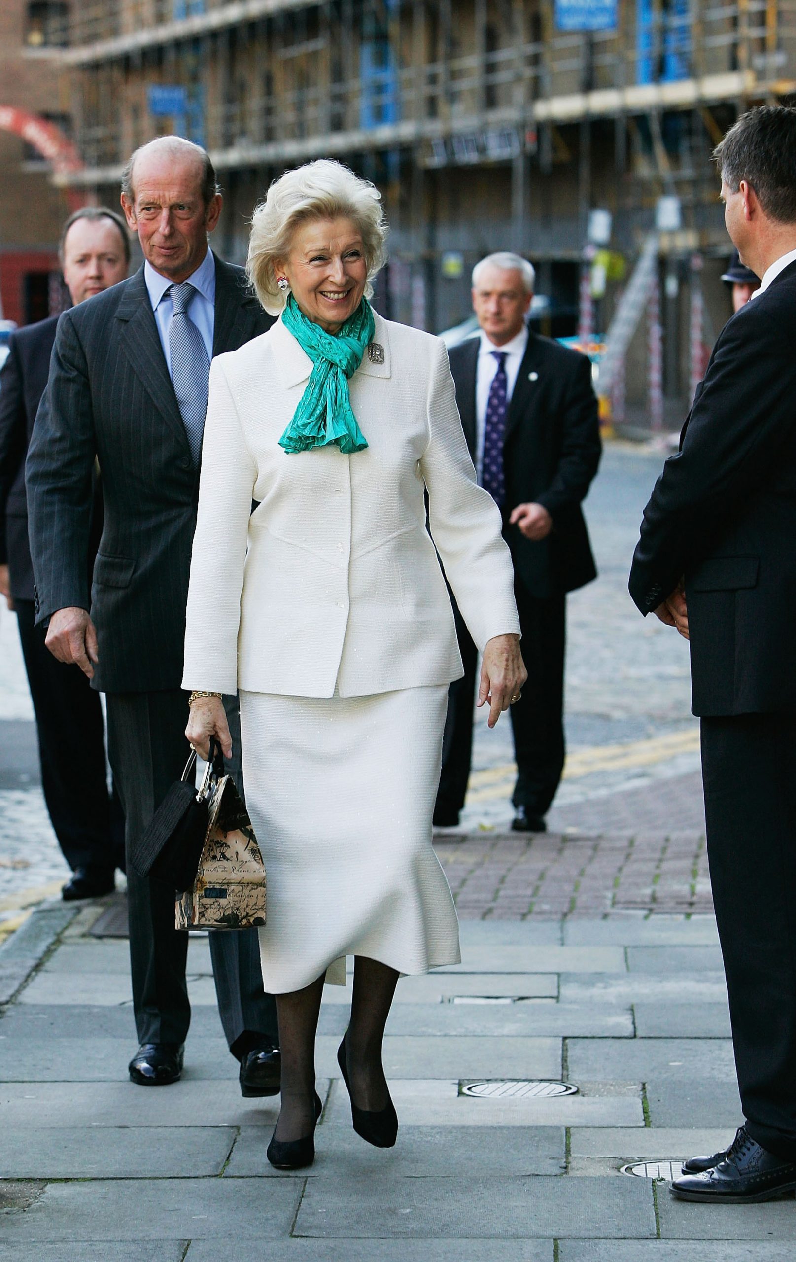 Glowing in crisp white and accented with a turquoise scarf, Princess Alexandra smiles graciously at a lunch hosted by the Norwegian Royal Family aboard their yacht on 27 October 2005. Walking just ahead of the Duke of Kent, she steps into the diplomatic moment with undeniable charm.