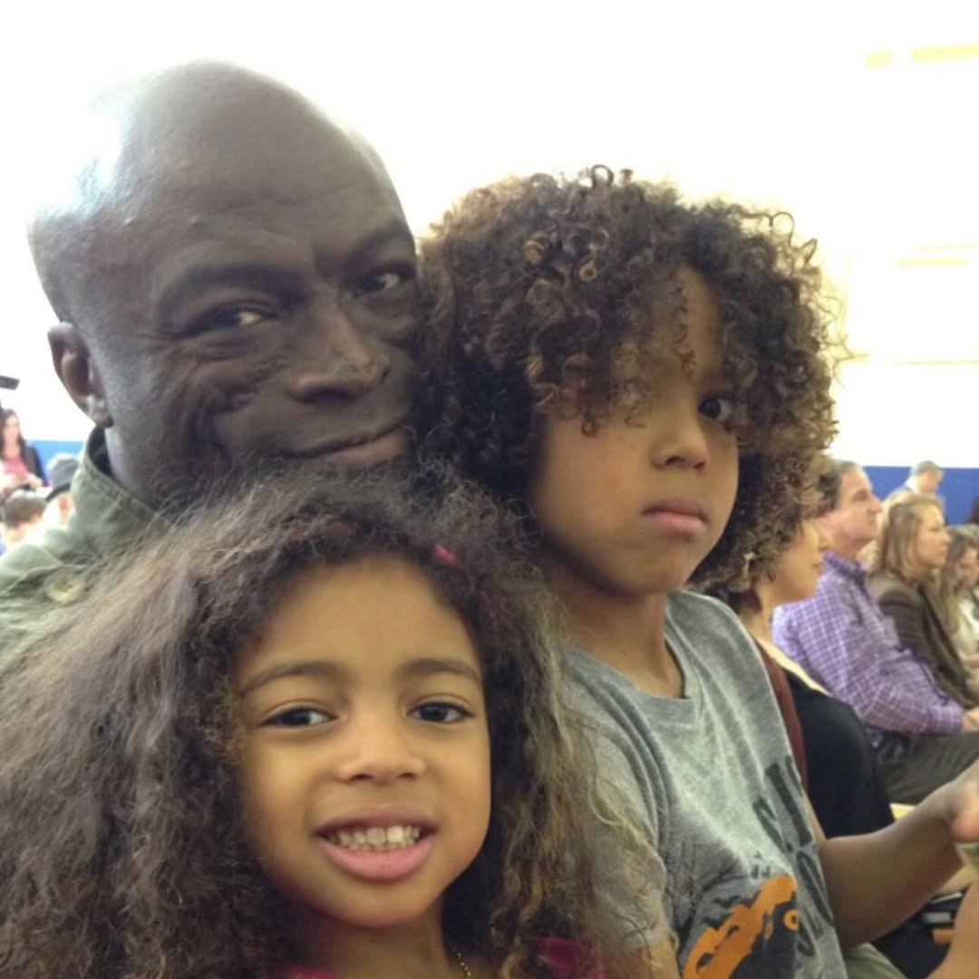 Johan Samuel sits beside his sister Lou Sulola Samuel and father Seal at a public event. He looks calmly toward the camera | Source: Instagram/j.smuel