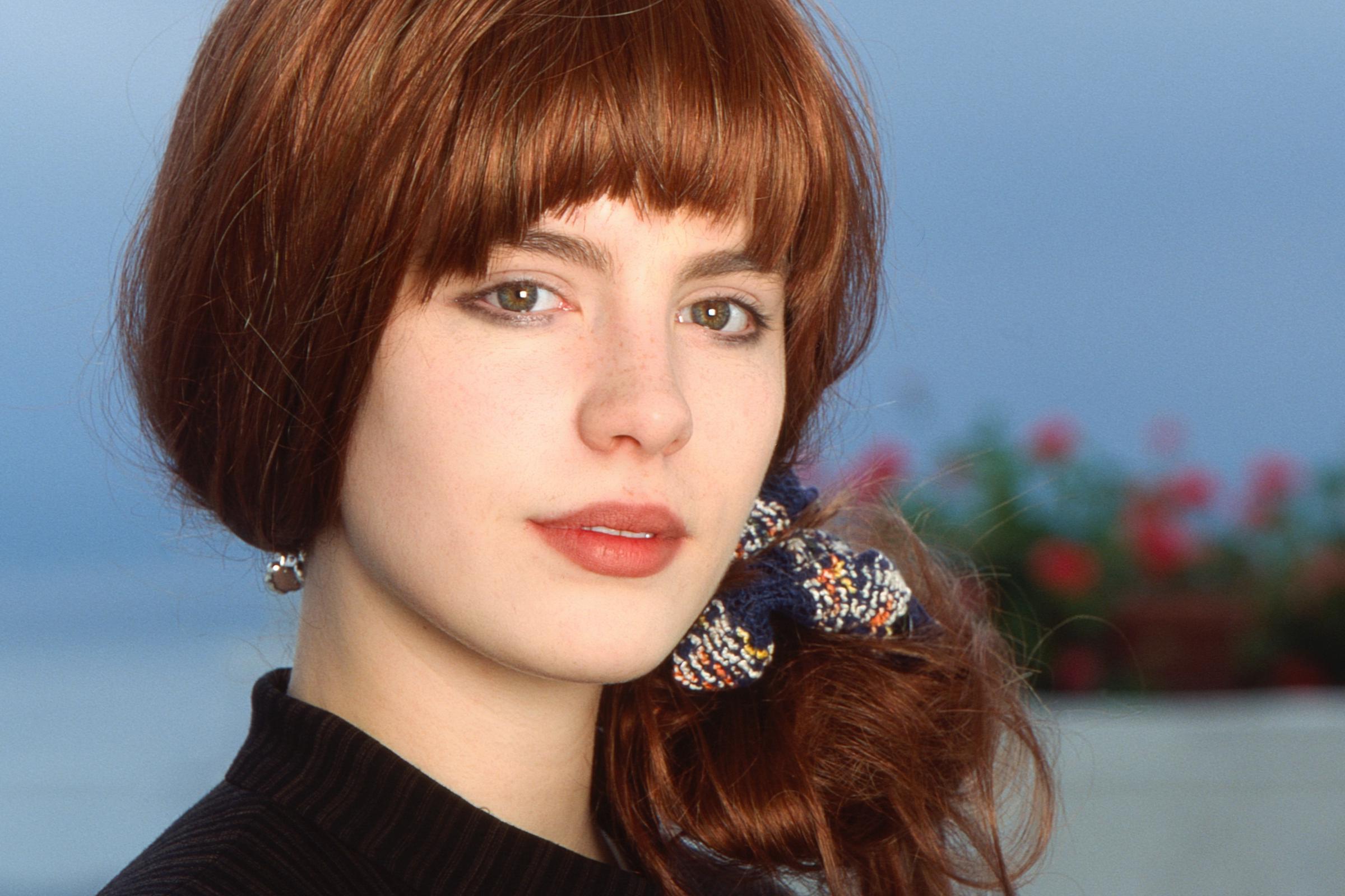 Kate Beckinsale is photographed early in her career, wearing her hair in a soft auburn style with fringe, reflecting the natural, understated look that marked her rise in the 1990s.