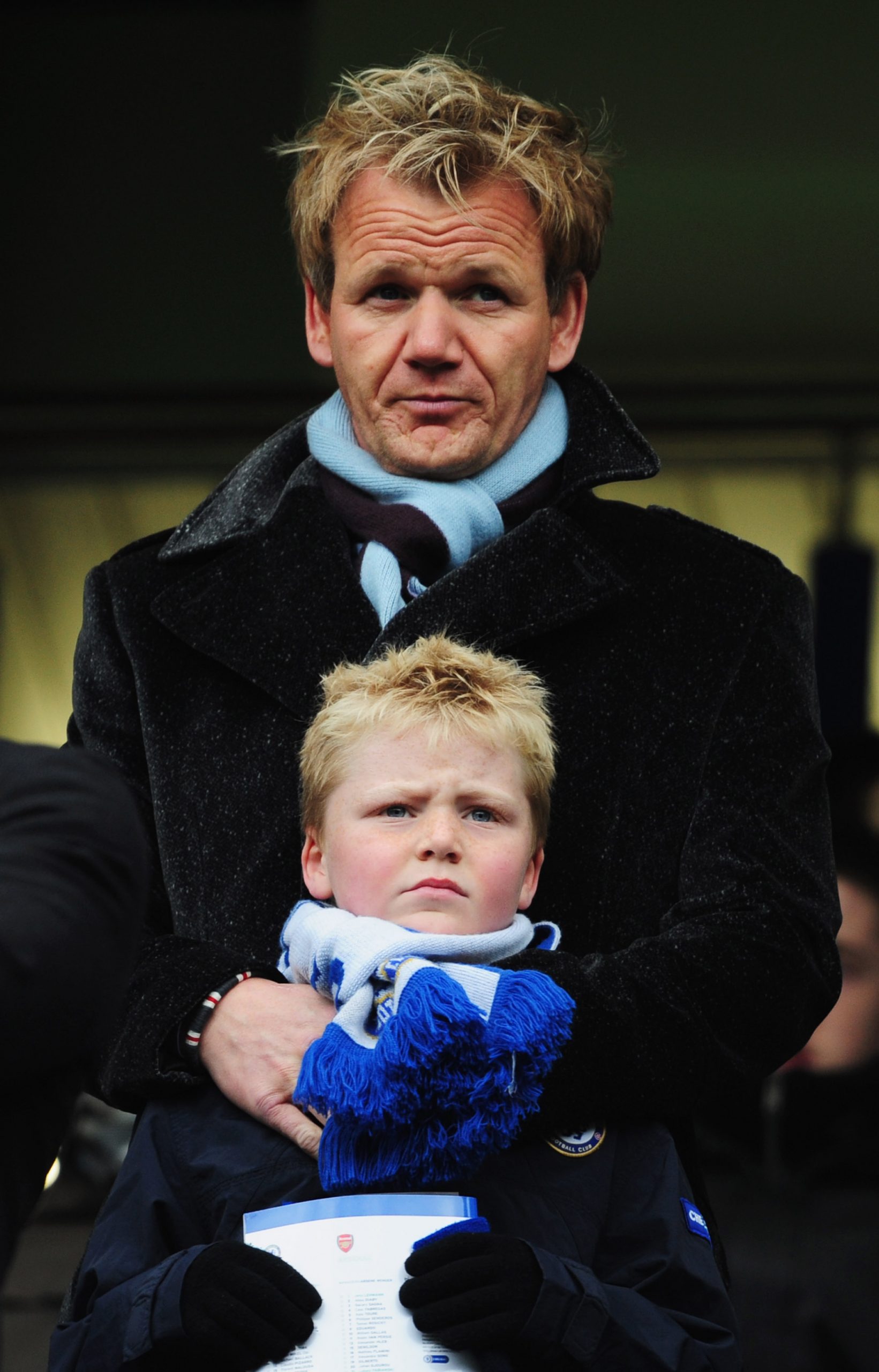A young Jack Ramsay stood in front of his father as the pair attended the Premier League match between Chelsea and Arsenal at Stamford Bridge on March 23, 2008. Wrapped in a blue scarf and gloves, Jack's serious expression reflected the intensity of the day, while Gordon's protective stance suggested the quiet bond they had long shared.
