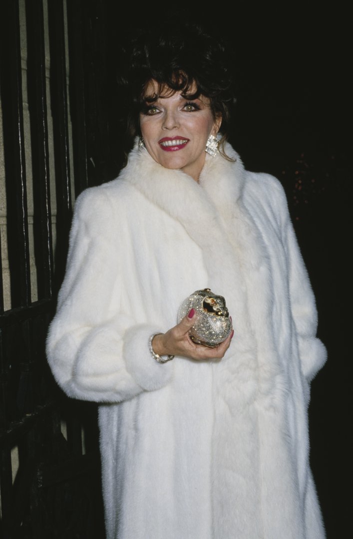 Wrapped in a white fur coat and framed by the glow of flashbulbs, Joan Collins stepped out in Los Angeles, California, circa 1980s, embodying the unapologetic opulence of the decade. With her crystal-studded clutch, statement earrings, and trademark glamour, she exuded the polished confidence that mirrored her defining role on primetime television during the era.