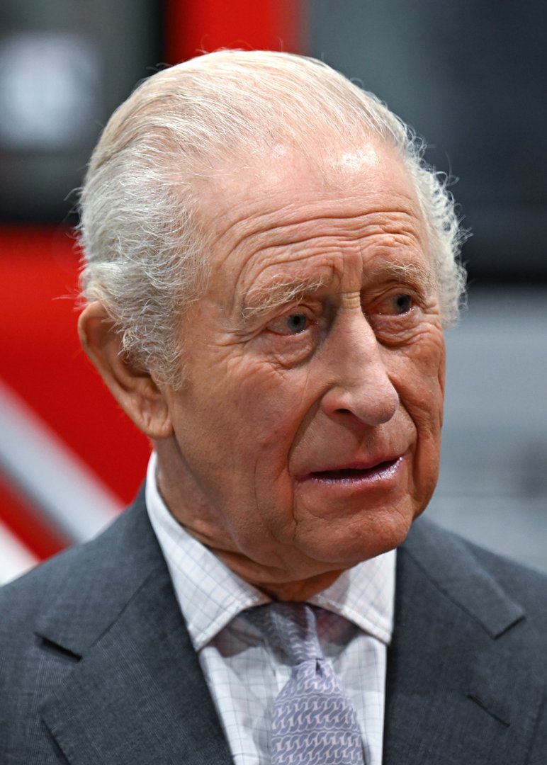 King Charles, photographed on 14 November 2025, appears with a concerned, slightly tense expression and is dressed in a grey suit, a checked shirt and a pale patterned tie.