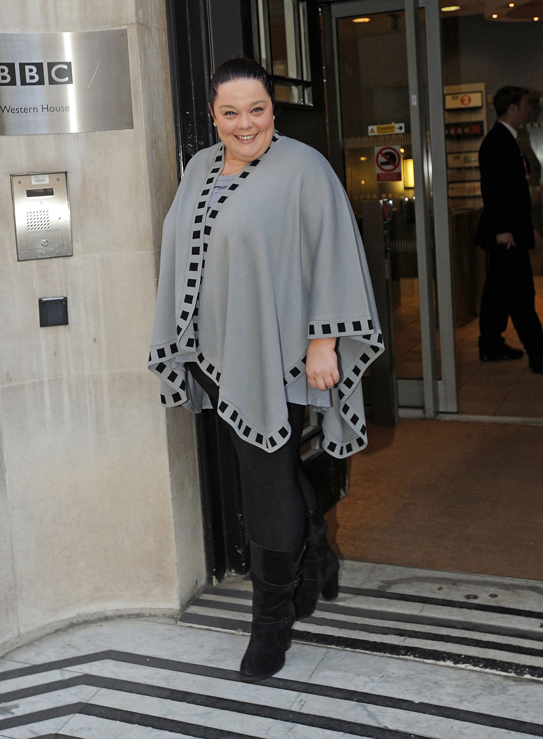 Radiant and ready for the spotlight! Lisa Riley beams outside BBC Radio 1 studios on 2 November 2012, wrapped in a chic grey cape and sleek all-black look as she commands attention at the iconic London landmark.