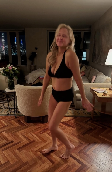 Wearing a revealing black bikini with a plunging neckline, Amy Schumer posed mid-step, smiling with eyes closed. Her toned stomach and noticeably firmer frame reflected the physical results of her 50-pound weight loss journey, captured without makeup or filters. | Source: Instagram/amyschumer