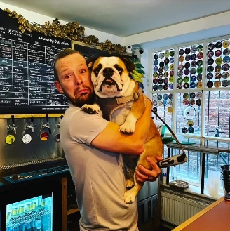 Adam Rickitt holding Daphne behind the bar in a light-hearted moment at their venue — from a post dated December 8, 2025. | Source: Instagram/katyrickitt