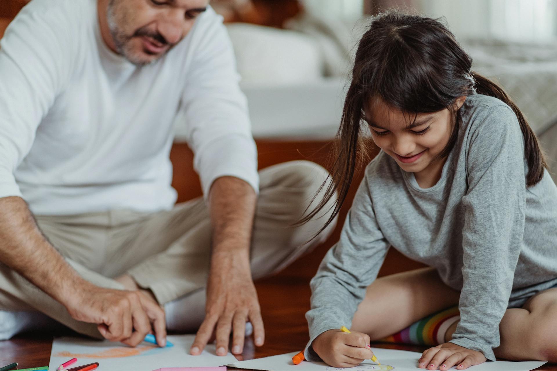 A father and his little girl sitting on the floor and coloring | Source: Pexels
