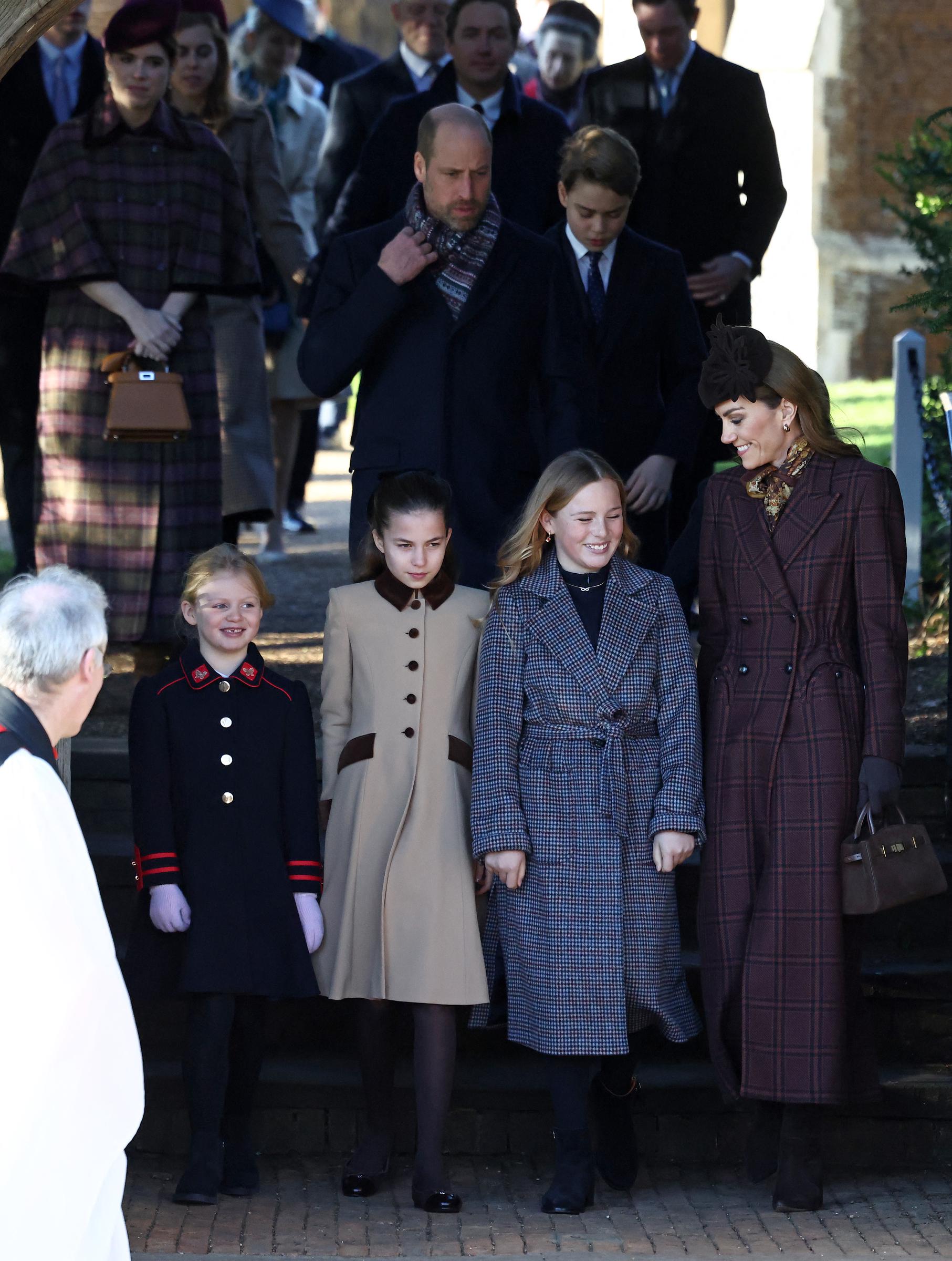 Catherine, Princess of Wales, smiles as she walks alongside children of the Royal Family, including Princess Charlotte, after the Christmas Day church service at Sandringham. Behind them, William, Prince of Wales, is seen adjusting his scarf &mdash; a gesture that body language experts later highlighted amid claims of social distance during the family gathering.
