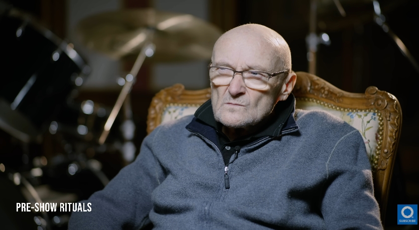 Phil Collins sits under soft stage lighting, his posture composed but his expression reflective. Now 74, the legendary musician has openly shared his struggles with mobility and health, and here, his thinning frame and serious gaze speak to a quieter chapter in his life away from touring and the spotlight. | Source: YouTube/Drumeo