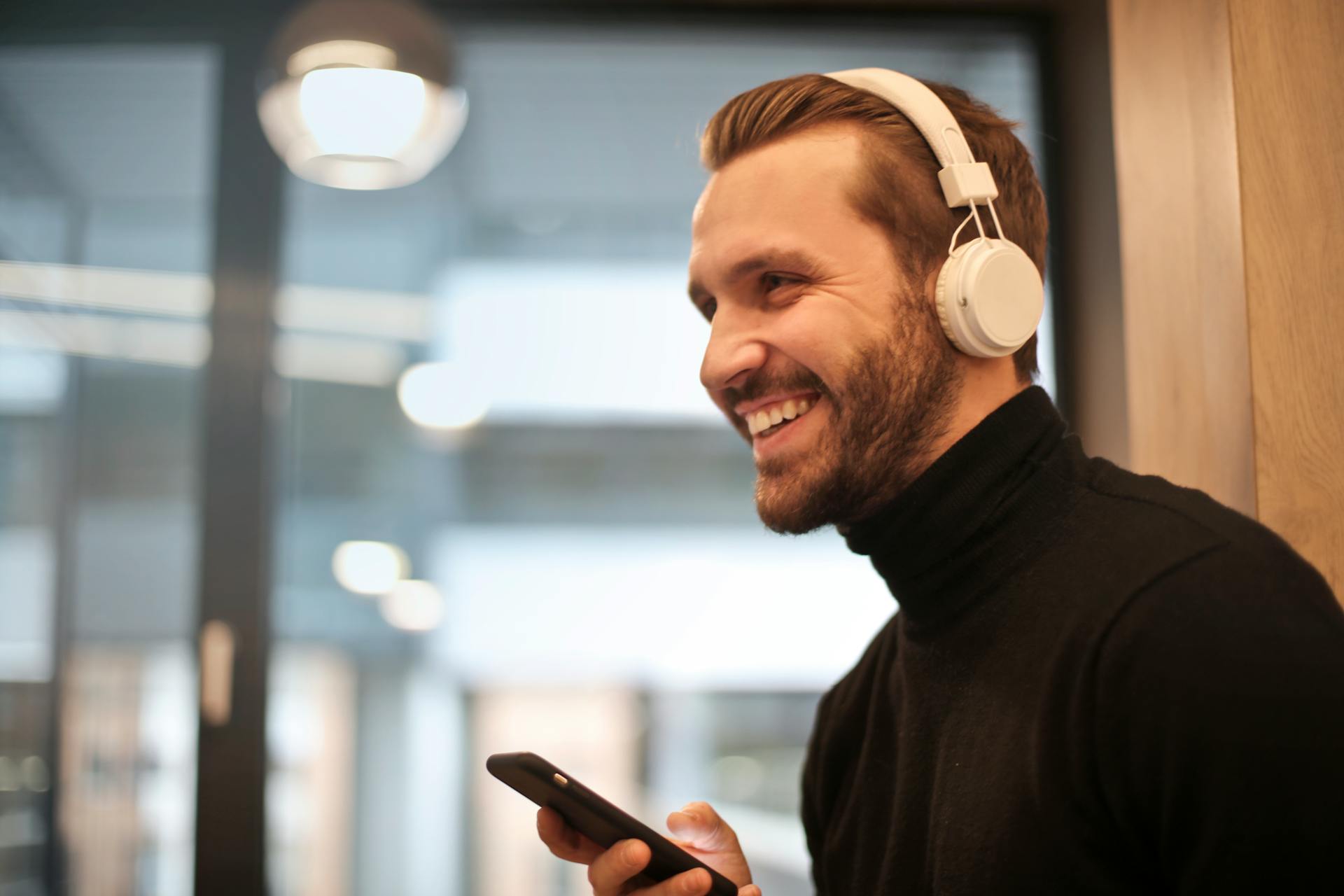 A smiling man wearing a white headset and holding his phone | Source: Pexels