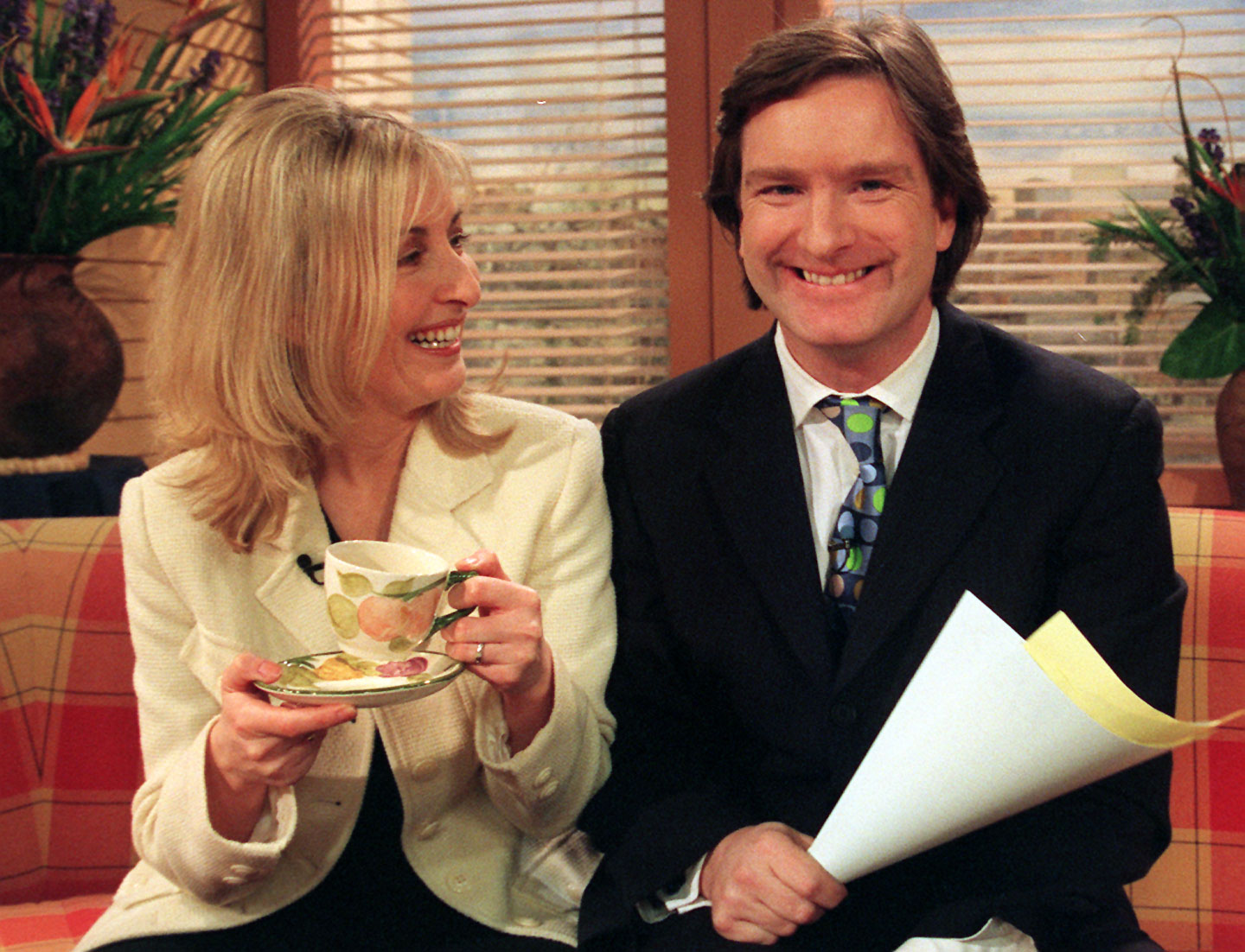 Fiona Phillips was pictured on the GMTV sofa in 1998 alongside a new co-host, her husband and reporter Martin Frizell, captured during a light-hearted on-air moment that reflected her ease in the studio and the rare crossover between their professional lives at a time when both were active figures in television journalism.