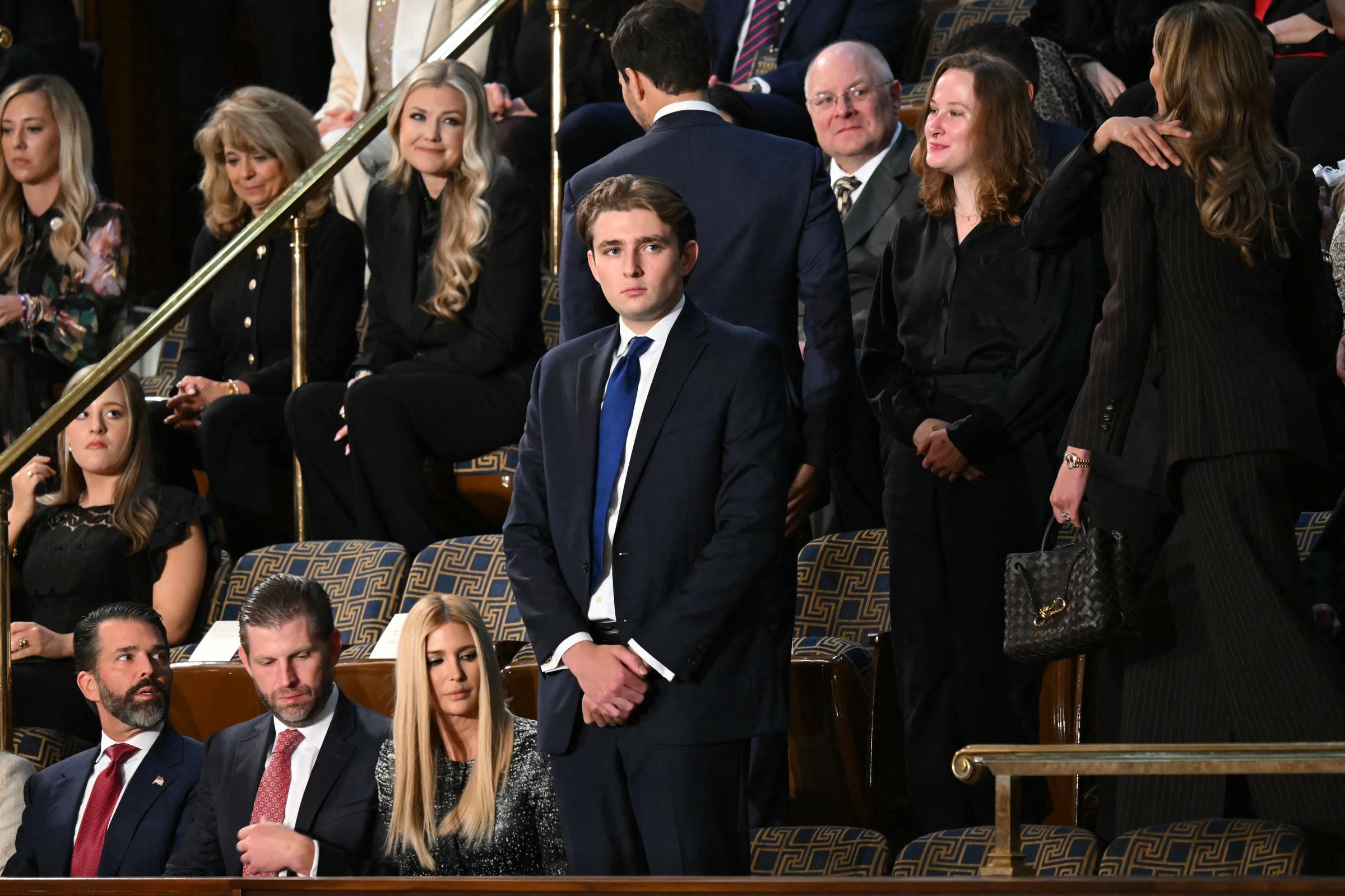 Barron Trump stands quietly in the House Chamber ahead of the State of the Union address in Washington, DC. Dressed in a navy suit and blue tie, he waits as guests settle into their seats around him. Members of the Trump family sit nearby as the chamber prepares for the President&rsquo;s arrival.