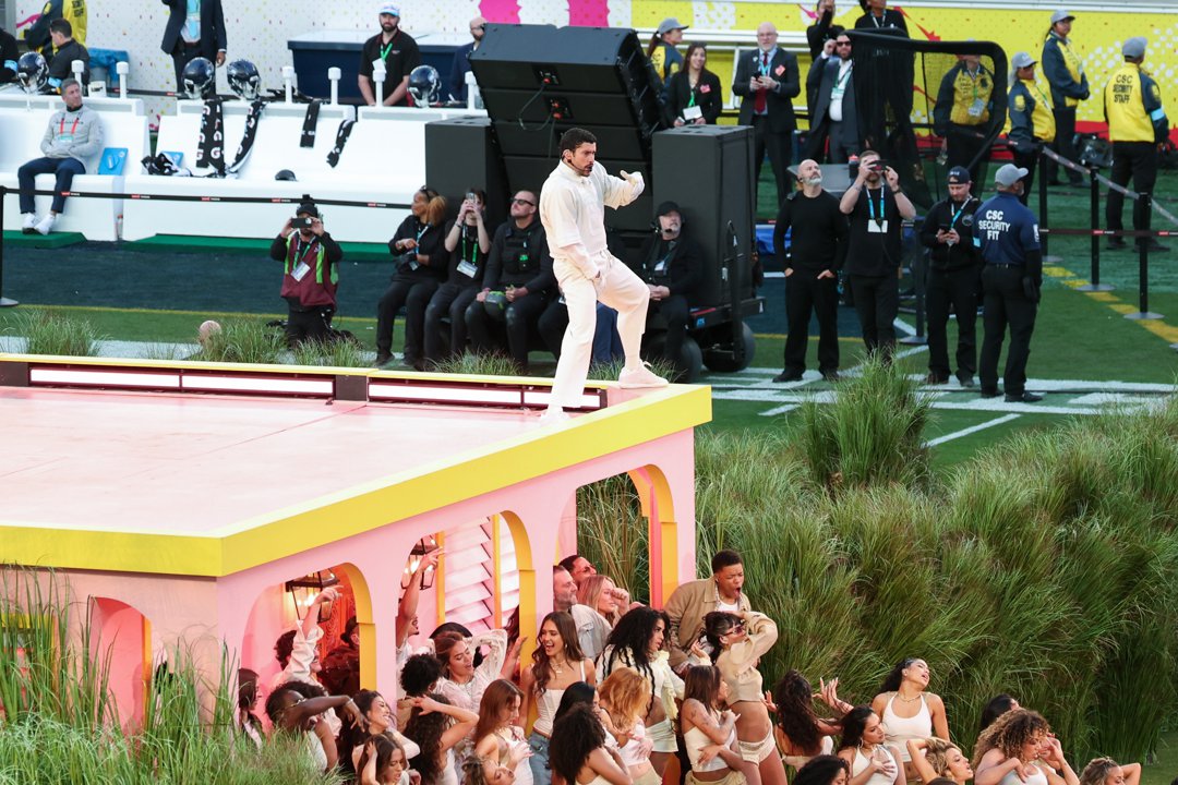 Bad Bunny performs atop a raised stage structure while dancers move below, creating a layered scene during the halftime performance.