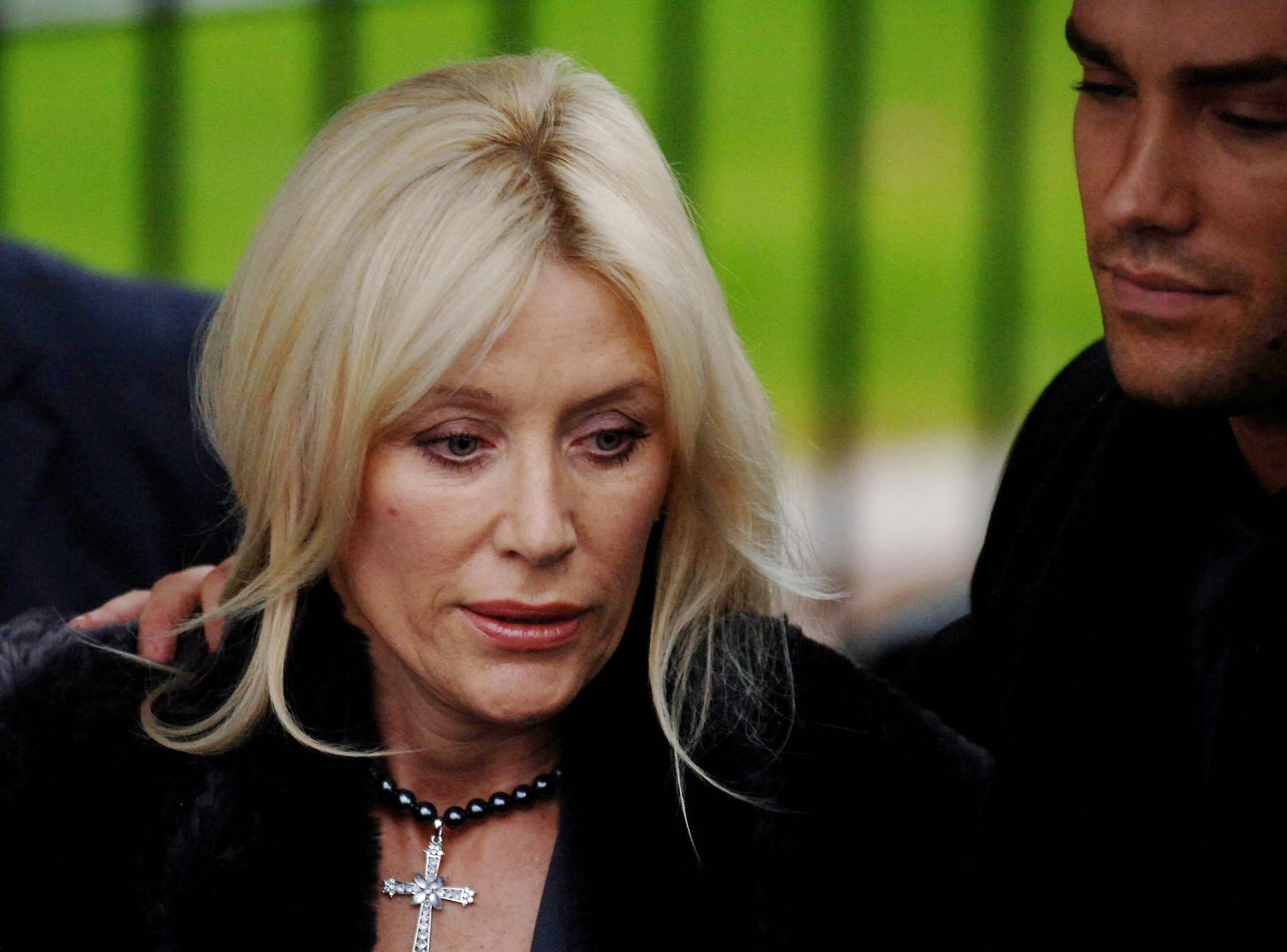 Angie is supported by her devoted son Calum as they arrive at Parliament Buildings in Stormont, Belfast, on Saturday 3 December 2005 for George Best&rsquo;s funeral. Composed yet visibly emotional, she stands with quiet dignity during a deeply solemn farewell, her strength evident as the city mourns one of its most celebrated sons.